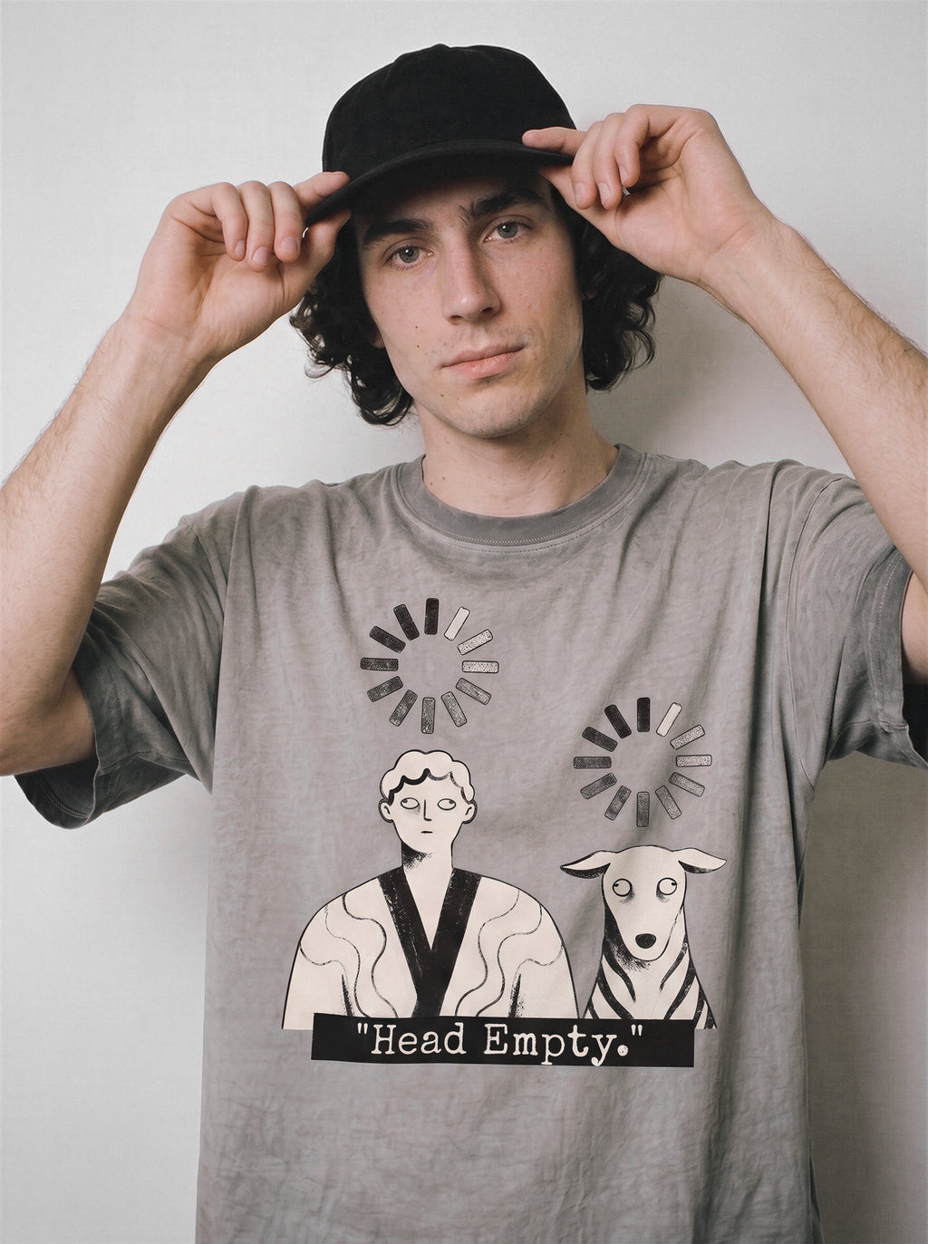 A male model adjusting his cap with both hands wearing an ombre grey head empty buffering icon graphic tee, capturing the brain drain state of mind.