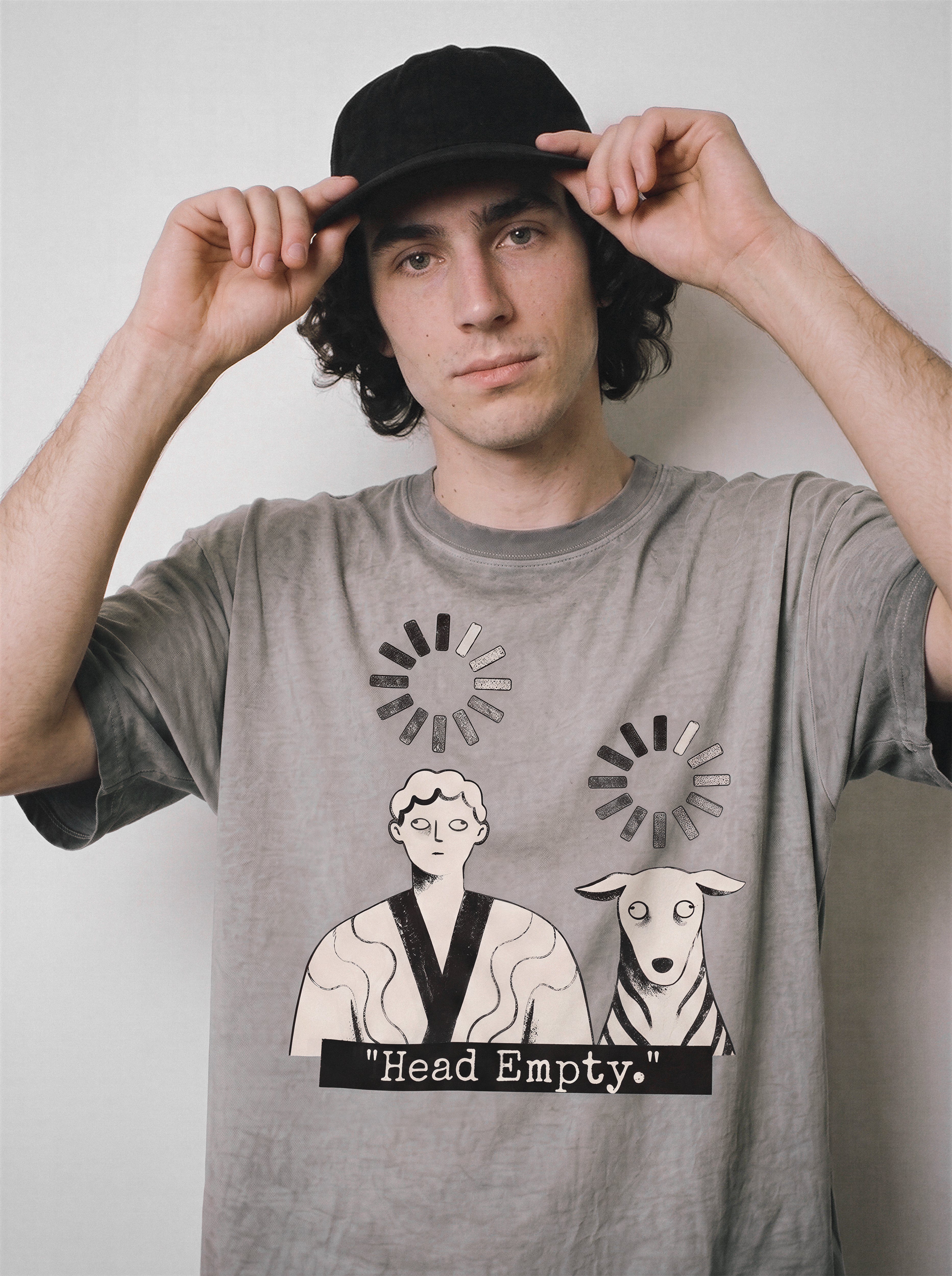 A male model adjusting his cap with both hands wearing an ombre grey head empty buffering icon graphic tee, capturing the brain drain state of mind.