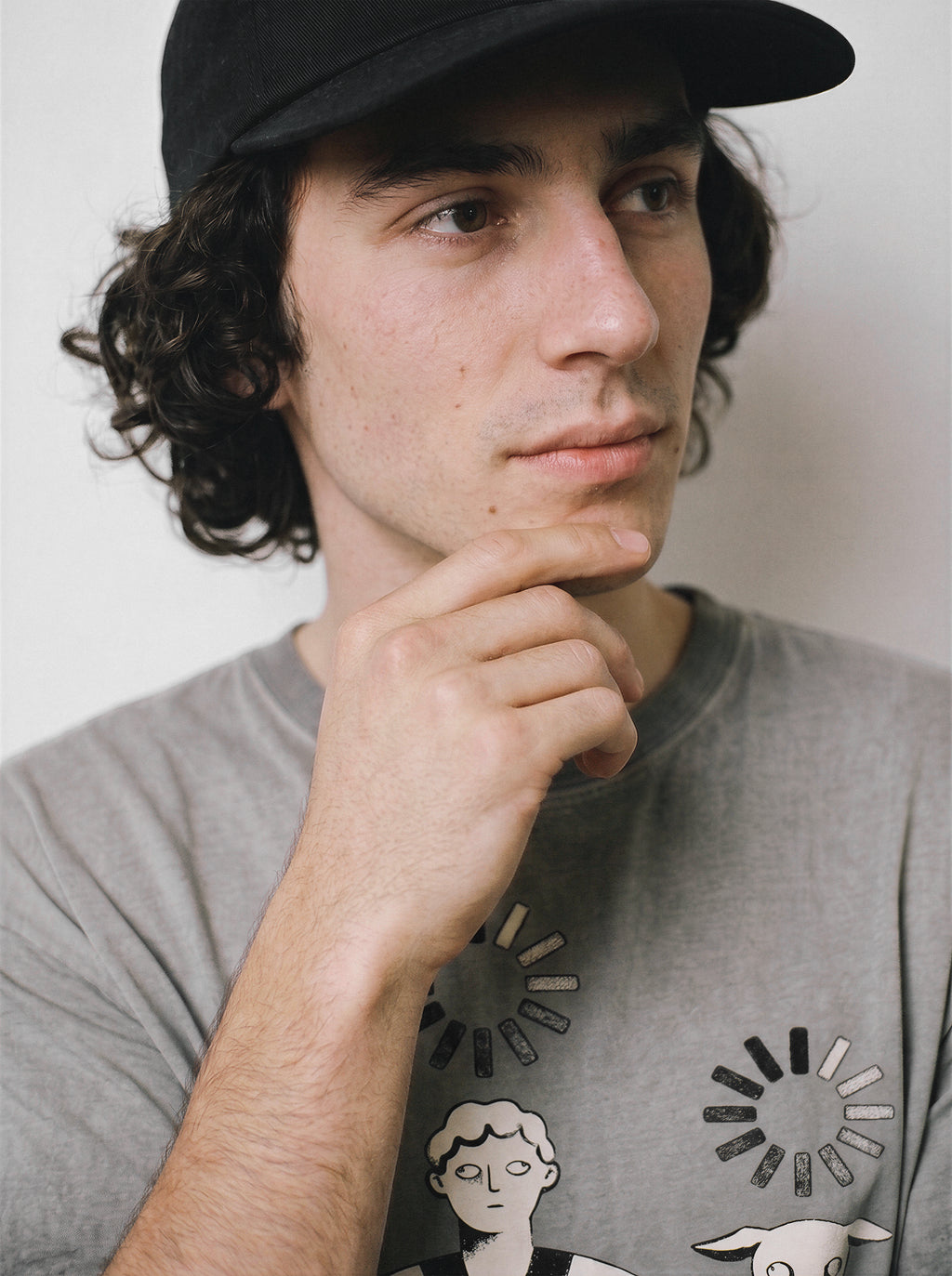 A close-up of a male model touching his chin wearing an ombre grey head empty buffering icon graphic tee, focusing on the deadpan boy and dog art.