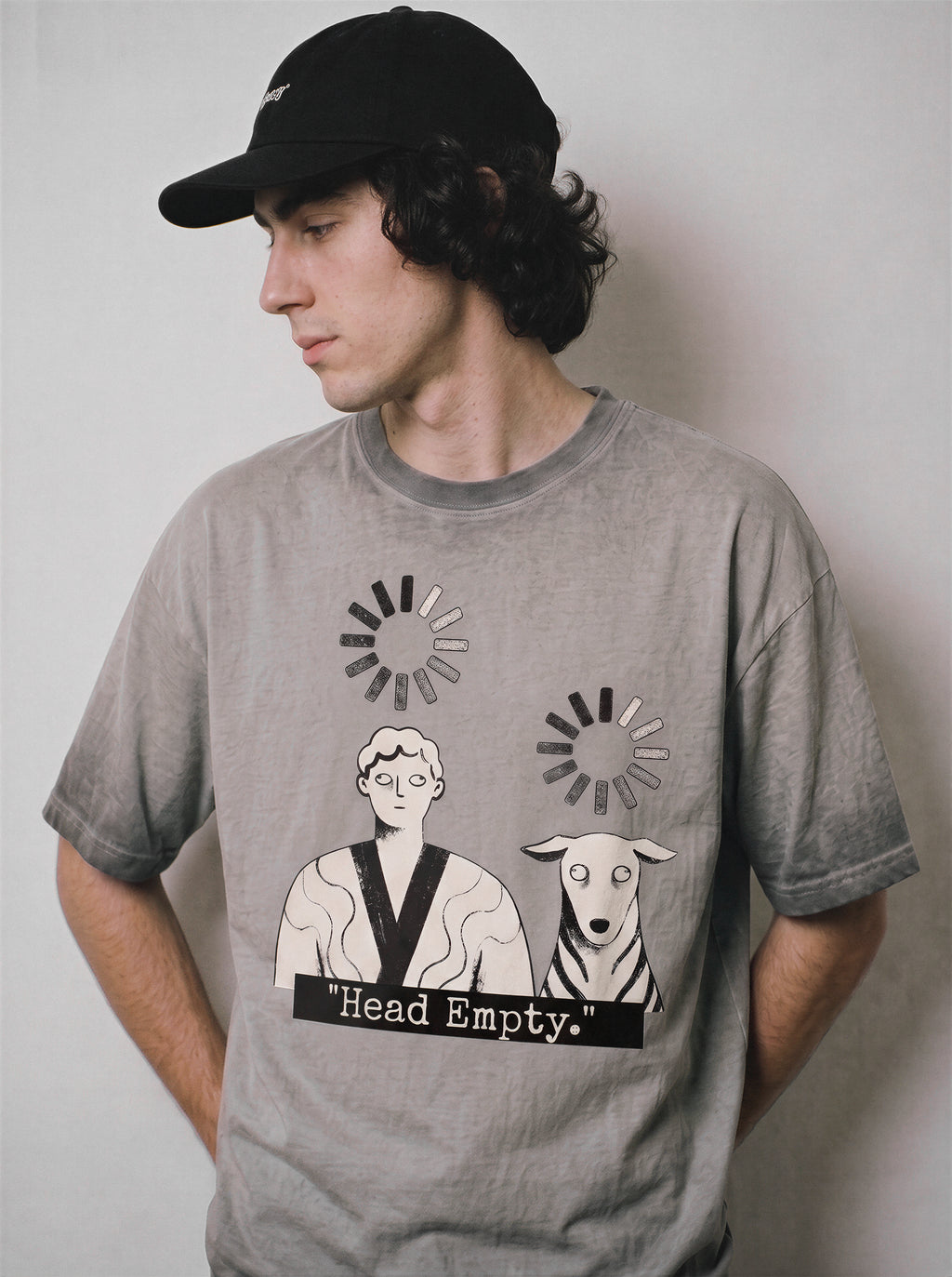 A male model looking down and aside wearing an ombre grey head empty buffering icon graphic tee, showcasing the existential offline mood and deadpan aesthetic.