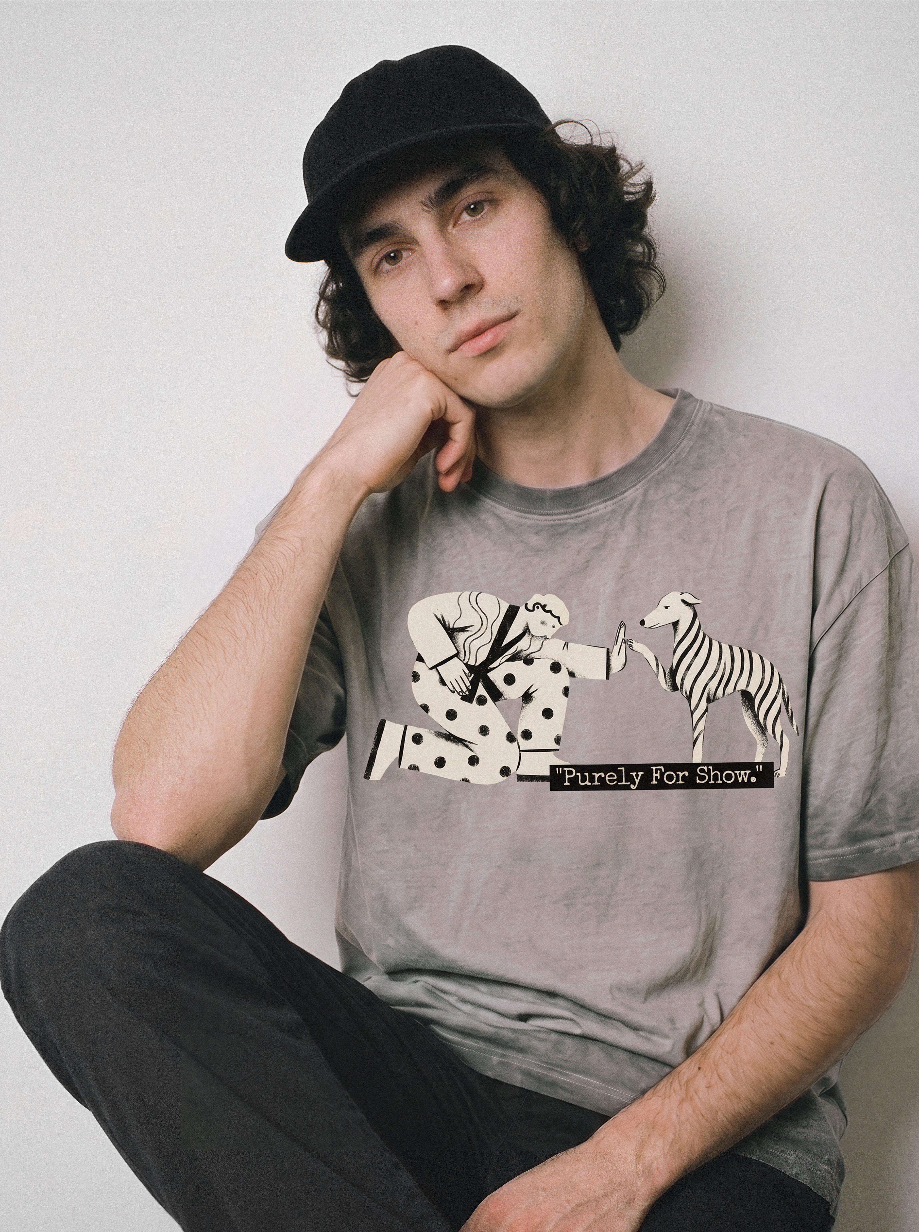 A seated male model resting his head on his hand wearing an ombre grey ironic high five graphic tee, highlighting the relatable going through the motions mood.