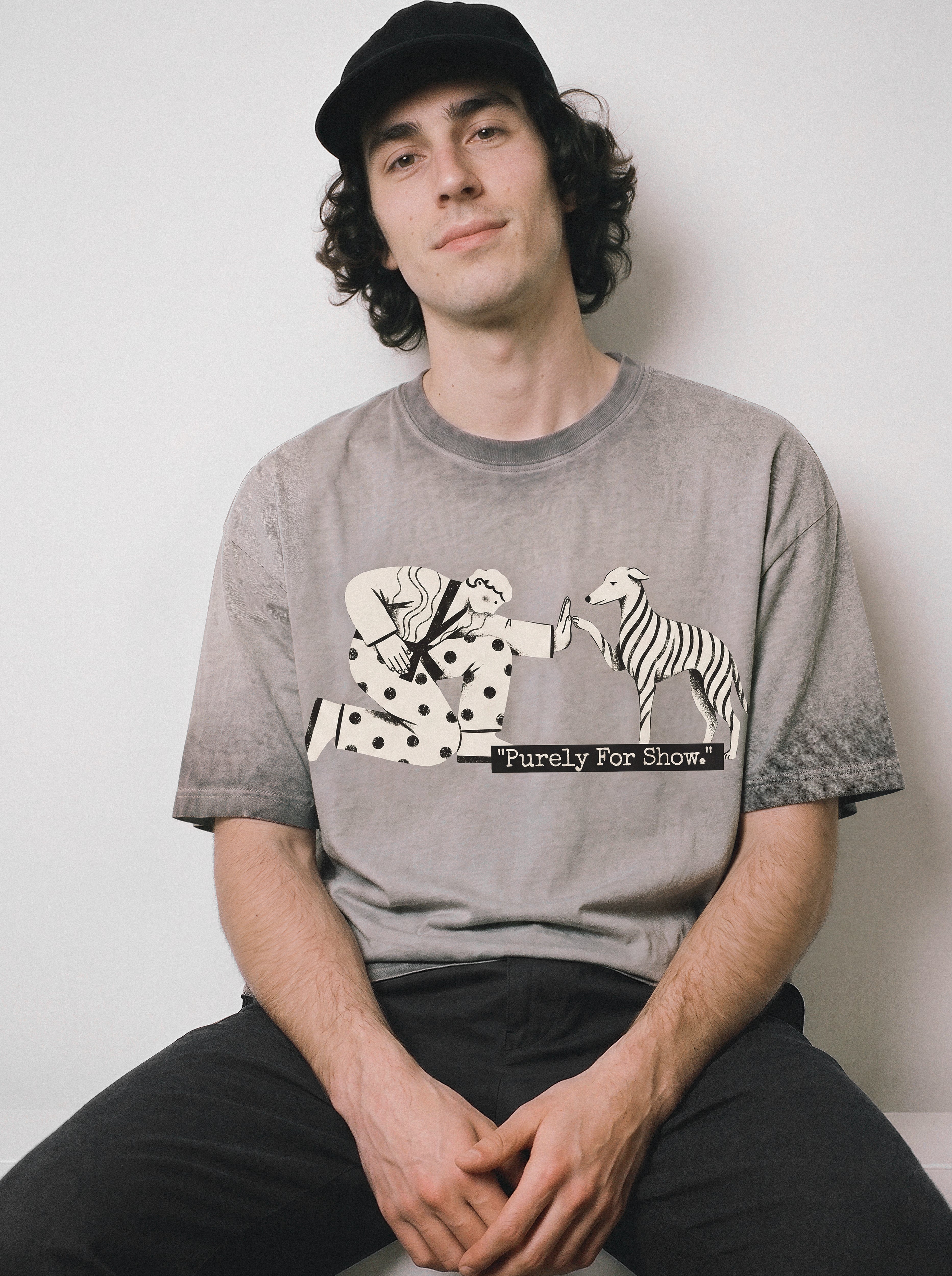 A seated male model looking forward wearing an ombre grey ironic high five graphic tee, capturing the dry humor and purely for show existential design.