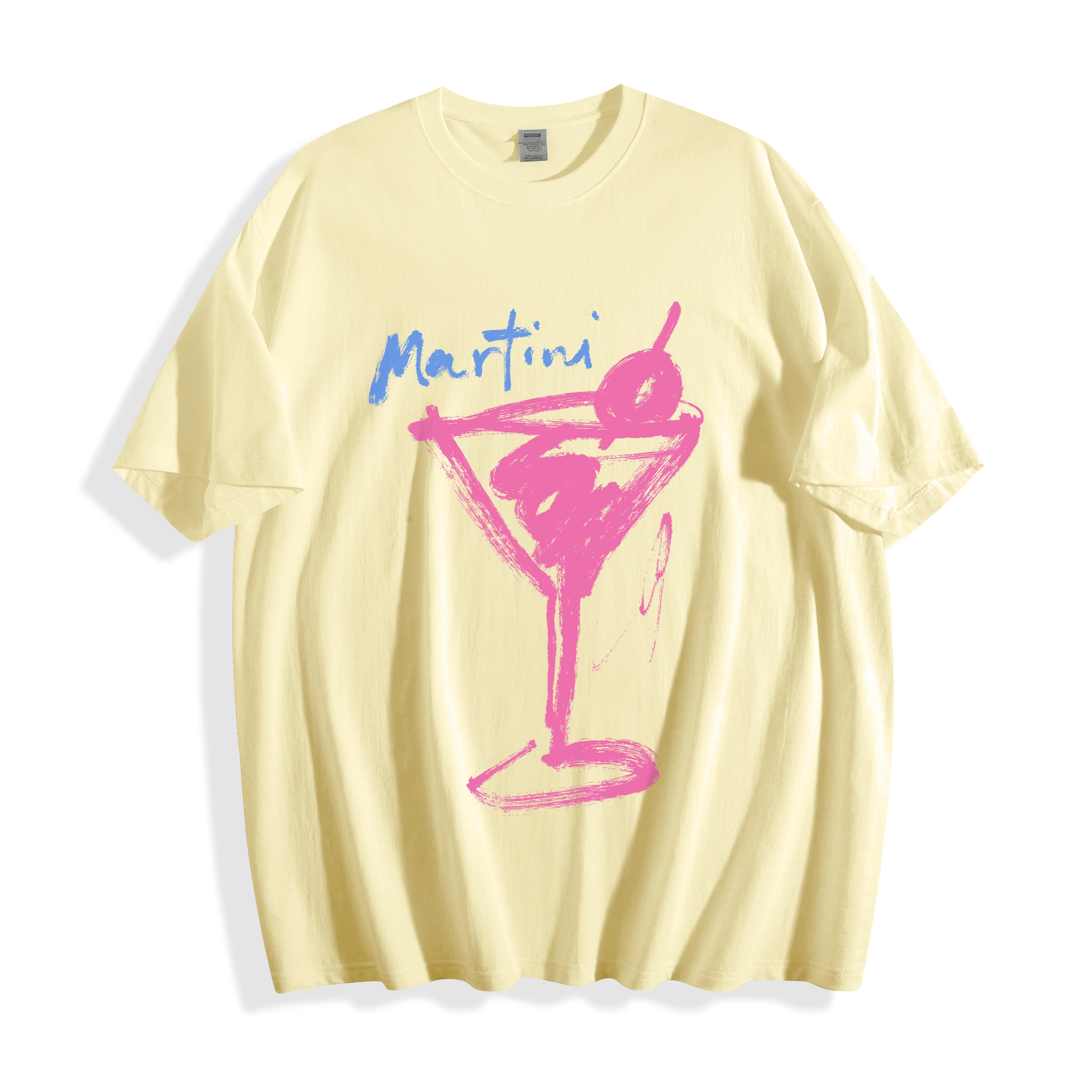 A pale yellow short-sleeve t-shirt with a pink and blue graphic on the front. The graphic features the word 'Martini' in blue script above a pink hand-drawn martini glass with a cherry on a cocktail stick.