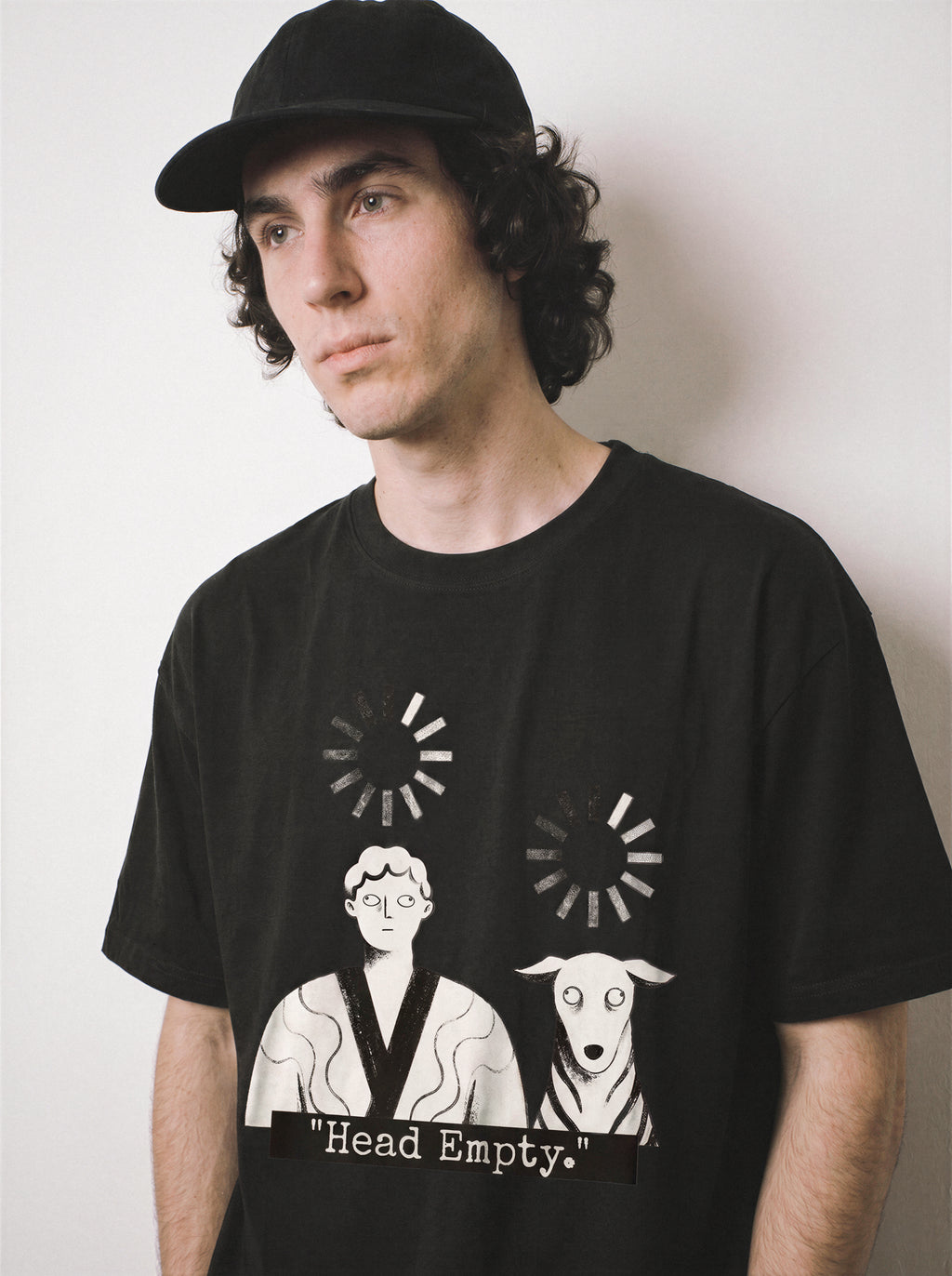 A male model looking aside with arms down wearing a black loading wheel graphic tee, emphasizing the brain drain aesthetic and casual drape.