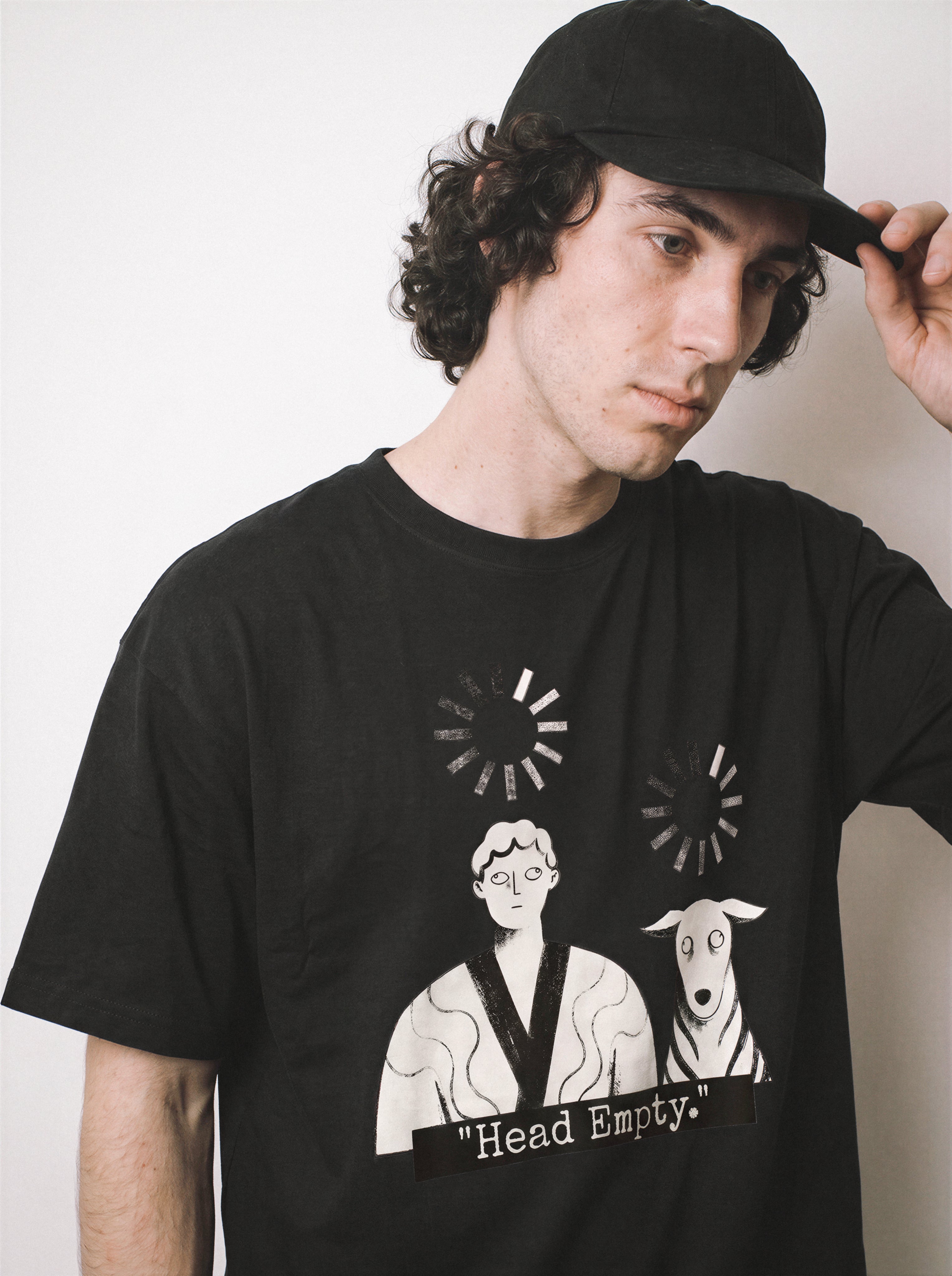 A close-up of a male model adjusting his cap wearing a black loading wheel graphic tee, showcasing the head empty print and buffering loading icons above a person and dog.