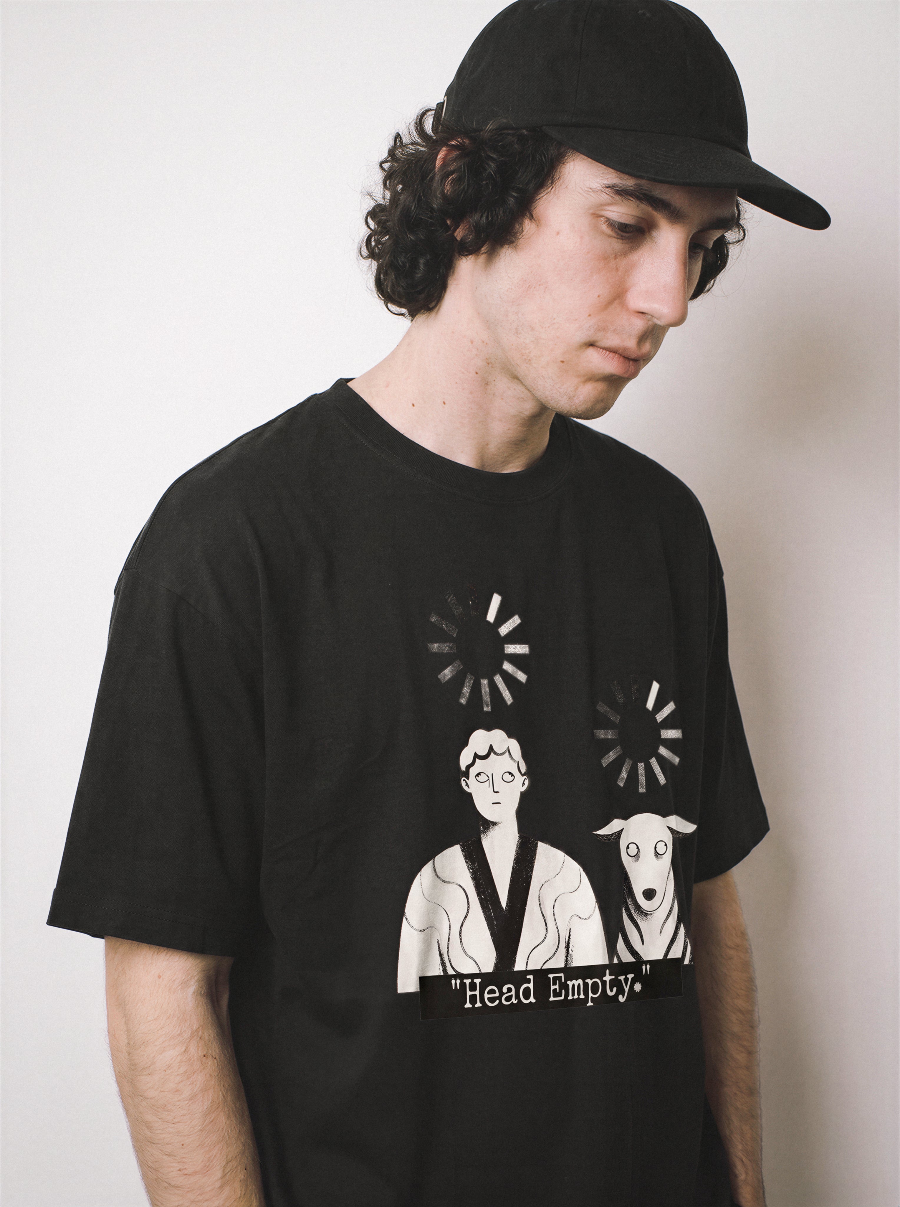 A male model standing sideways looking down wearing a black loading wheel graphic tee, capturing the complete offline mood and introvert streetwear style.