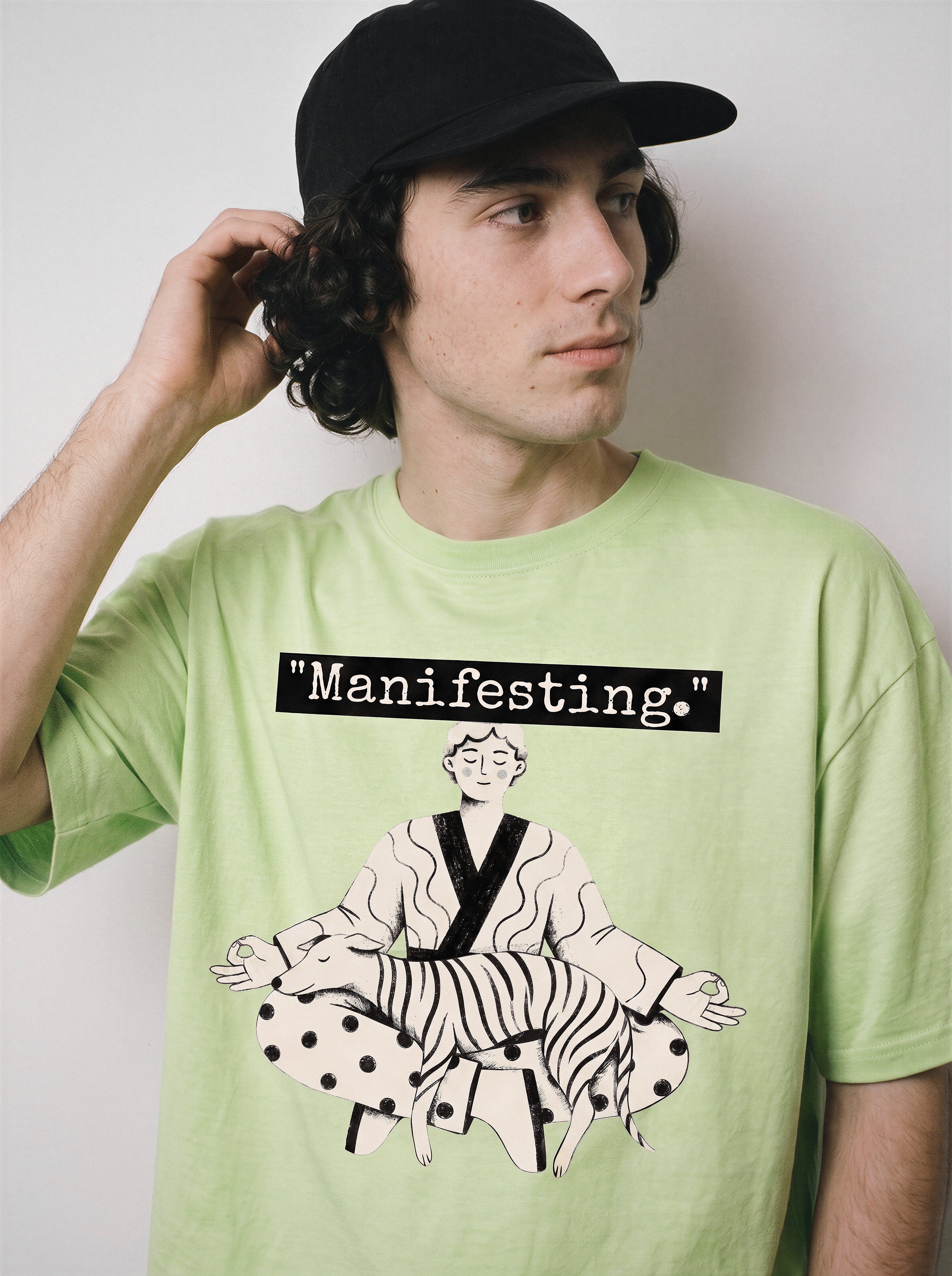 A male model looking away with his hand behind his head wearing an acid lime manifesting meditating graphic tee, highlighting the line art print and detached mindfulness aesthetic.