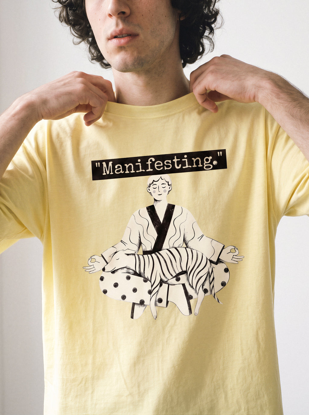 A male model adjusting his collar wearing a butter yellow meditating boy and dog line art graphic tee, capturing the distinctive quirky graphic design.