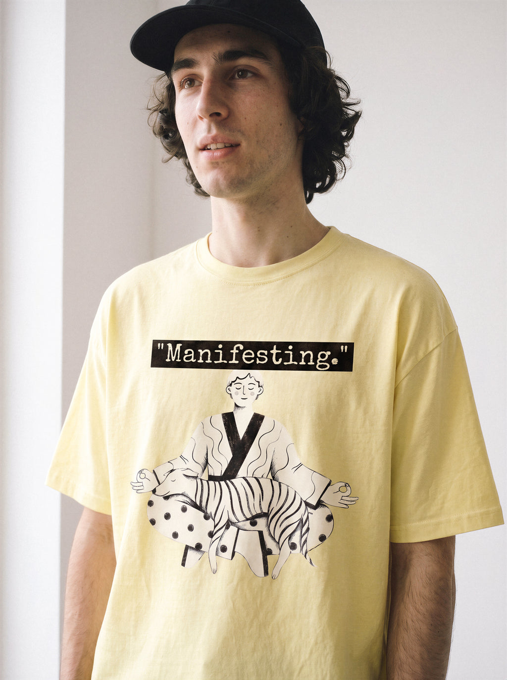 A half-body shot of a male model looking away wearing a butter yellow meditating boy and dog line art graphic tee, displaying the bold line art streetwear style.