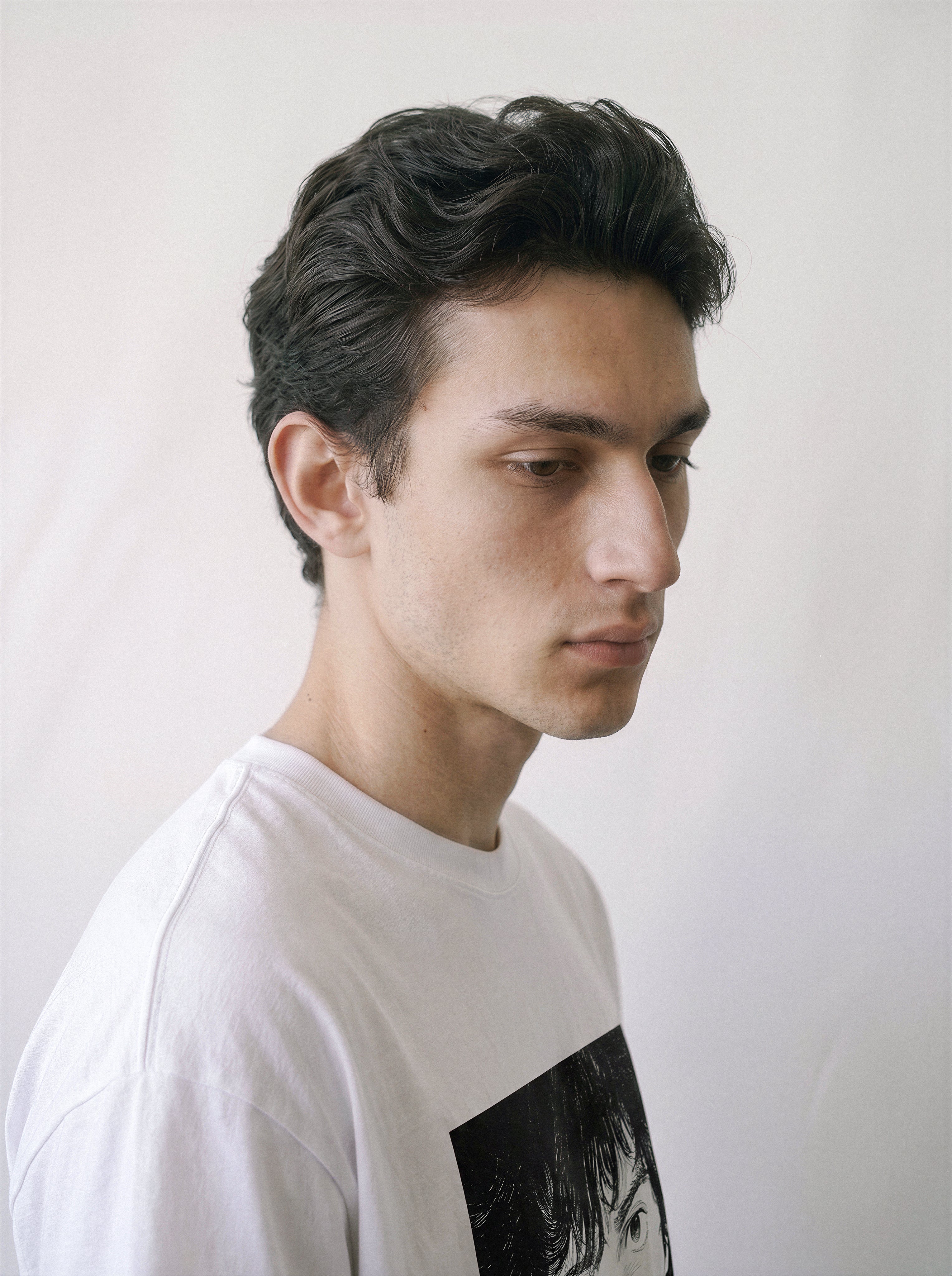A side profile of a male model wearing a white messy hair manga portrait graphic tee, demonstrating the striking monochrome illustration and minimalist streetwear look.