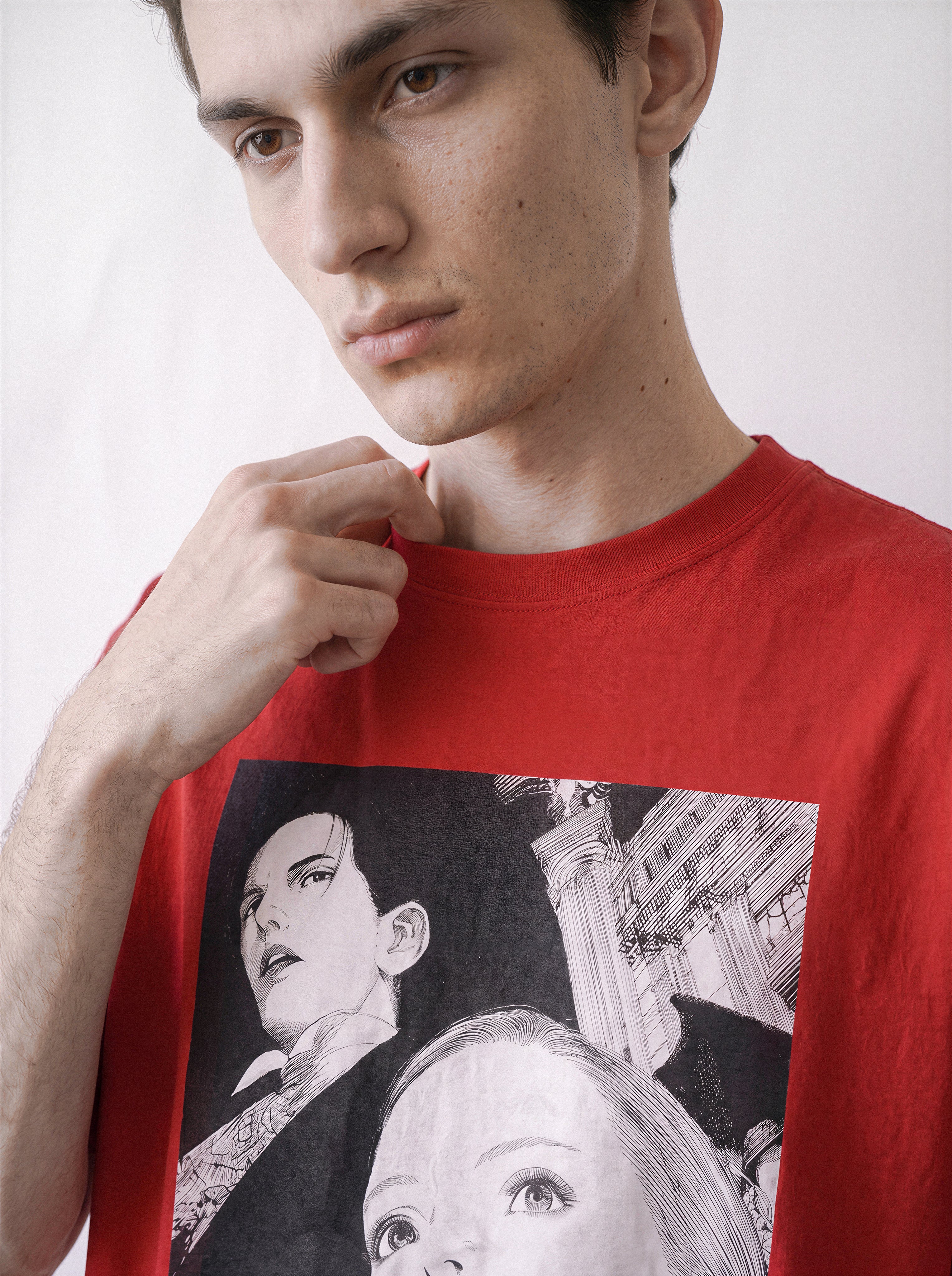 A close-up of a male model touching his collar wearing a red monochrome upward gaze graphic tee, focusing on the sharp line art and classical architectural elements.