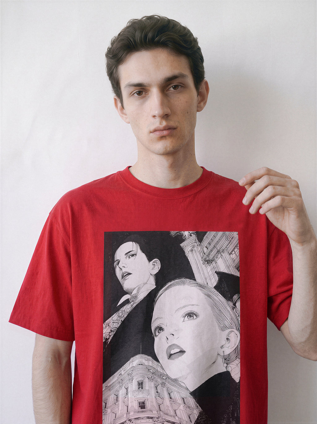 A male model touching the hem wearing a red monochrome upward gaze graphic tee, highlighting the high-contrast portrait graphic against a bold colorway.