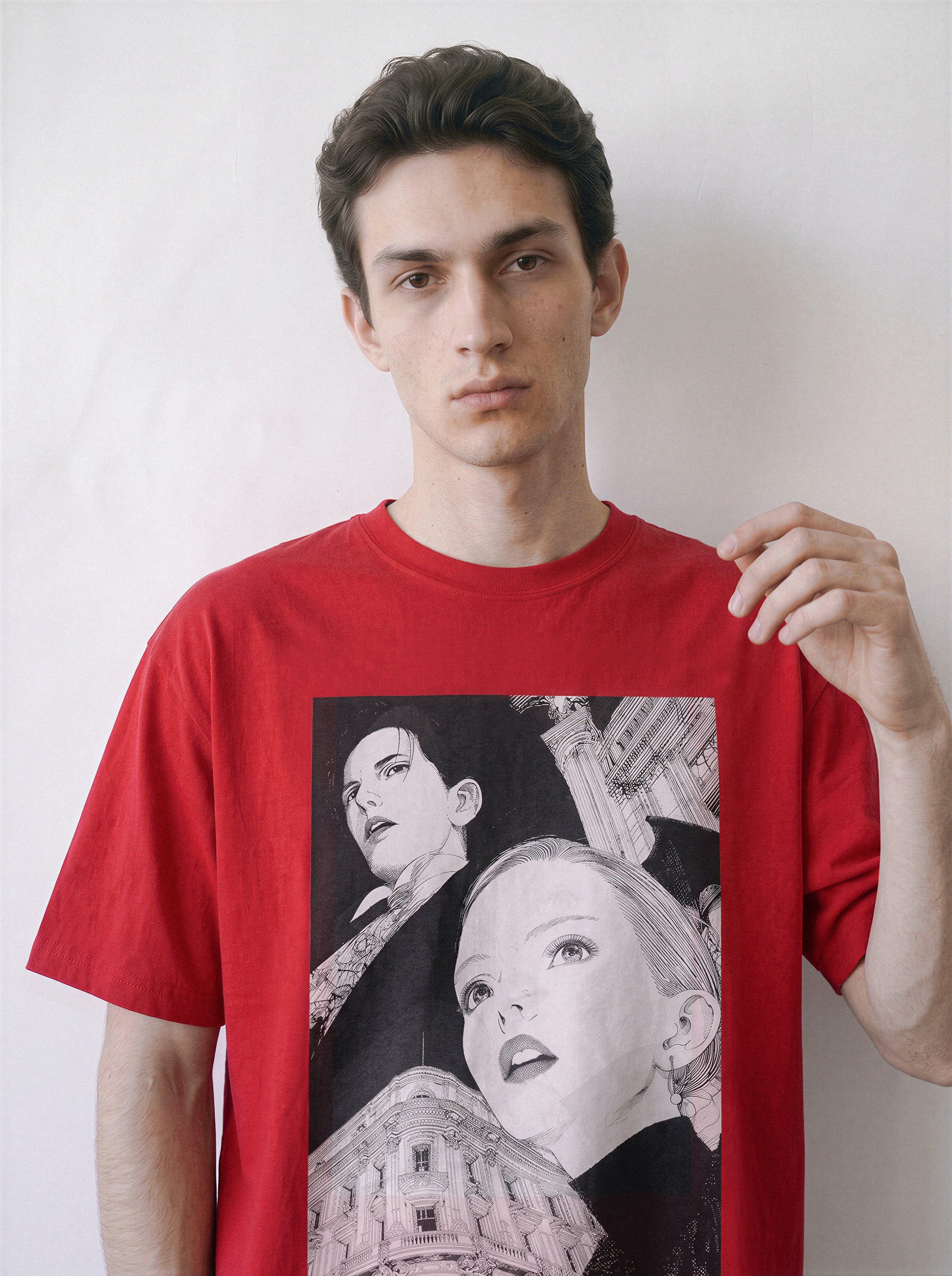 A male model touching the hem wearing a red monochrome upward gaze graphic tee, highlighting the high-contrast portrait graphic against a bold colorway.