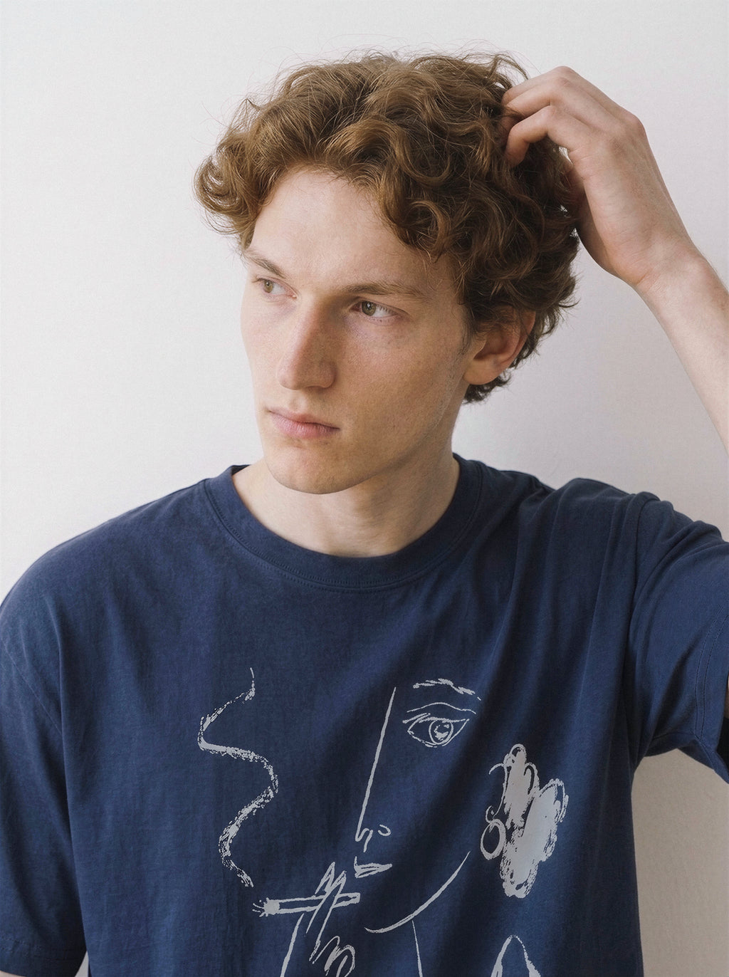 Close-up shot of a model with his hand in his hair, emphasizing the chalk-textured smoking figure graphic on a navy oversized t-shirt.