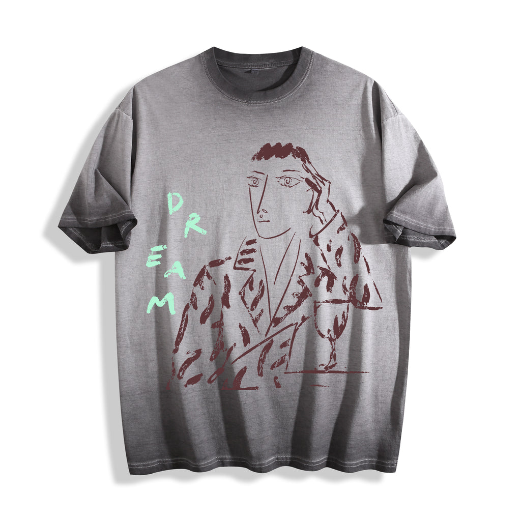 Flat lay product photography of an ombre grey heavyweight boxy fit t-shirt showcasing a sharp charcoal-like portrait sketch and hand-lettered DREAM typography.
