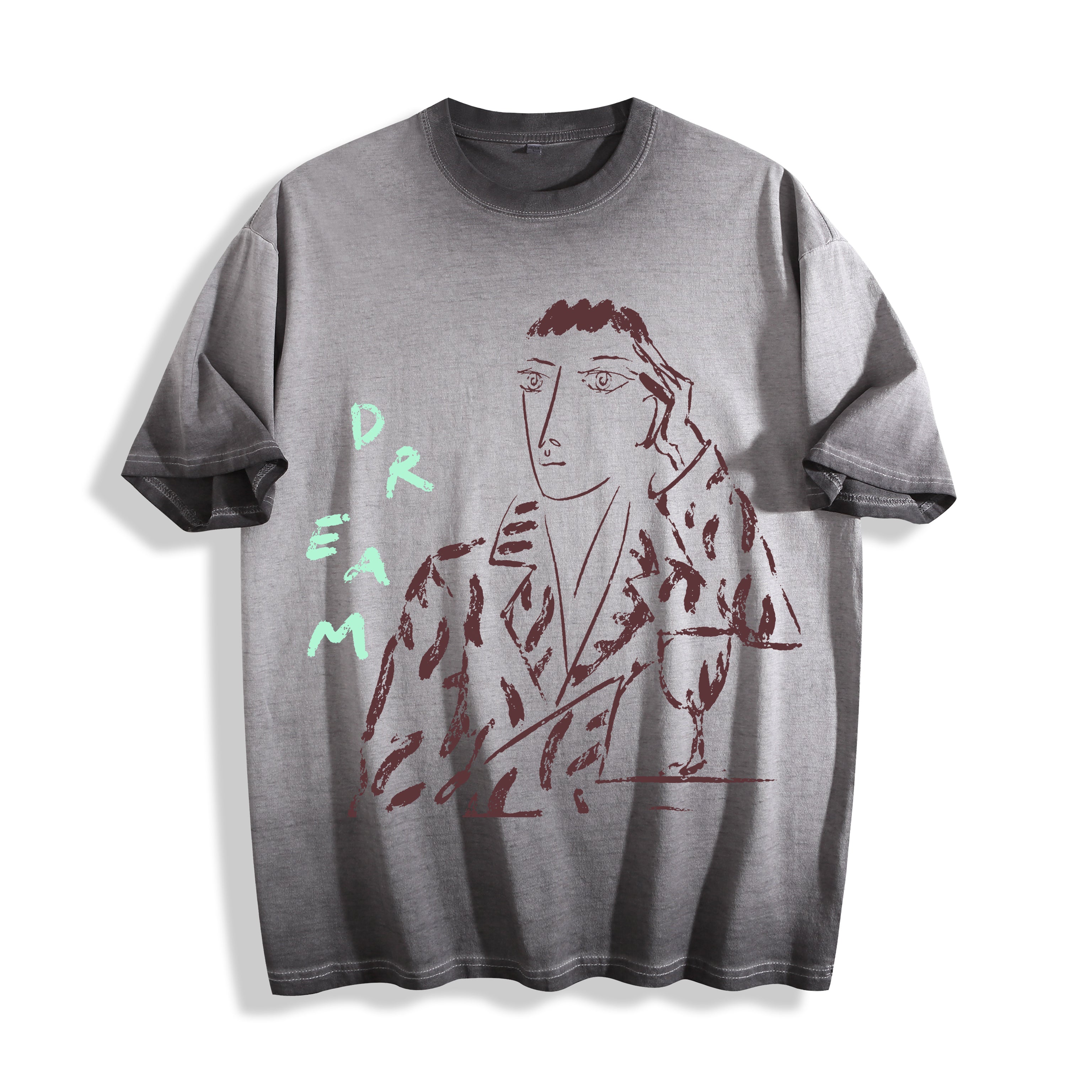Flat lay product photography of an ombre grey heavyweight boxy fit t-shirt showcasing a sharp charcoal-like portrait sketch and hand-lettered DREAM typography.