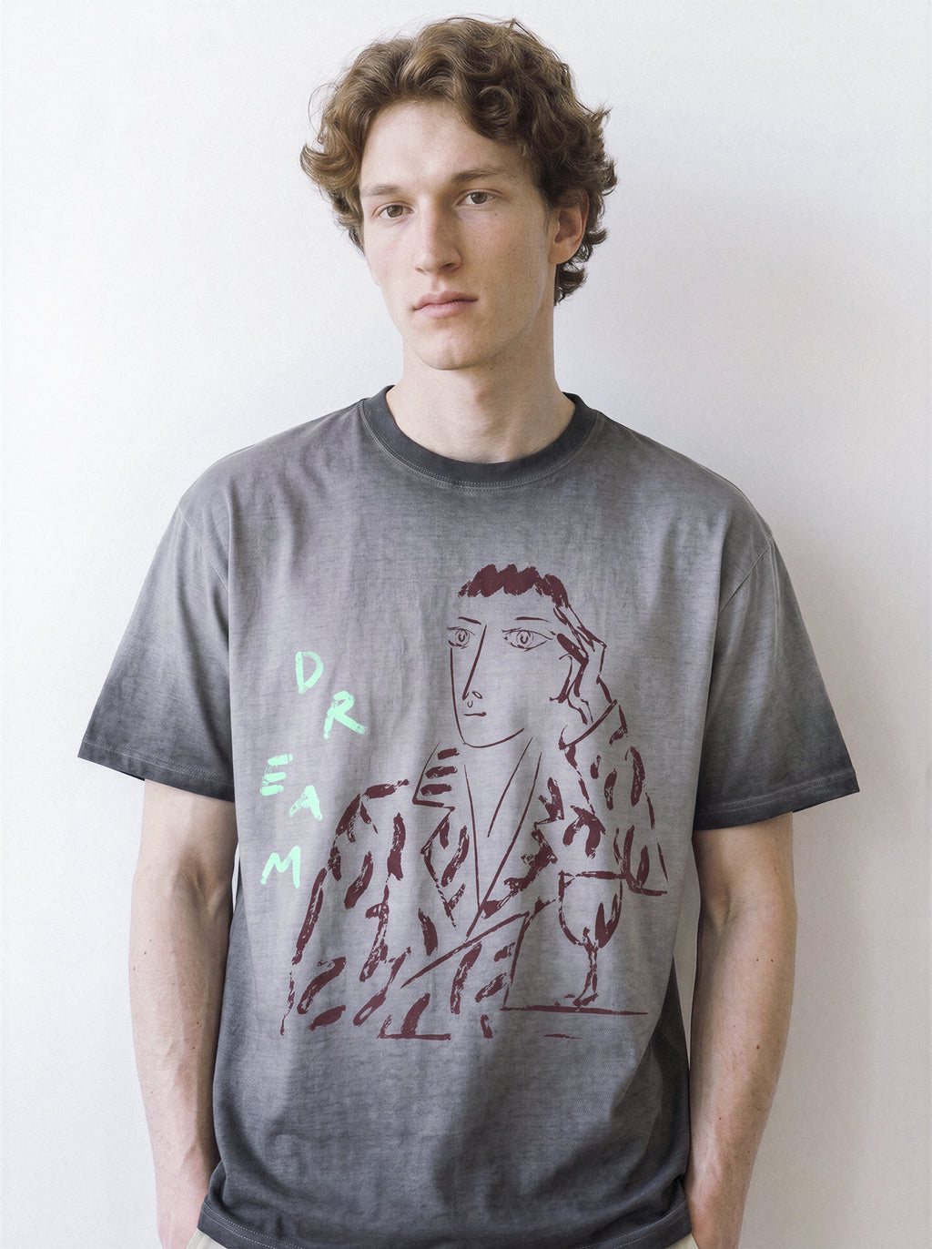 Front view of a male model standing naturally, demonstrating the structured drape of an ombre grey 230g premium cotton tee with a daydreamer charcoal sketch design.