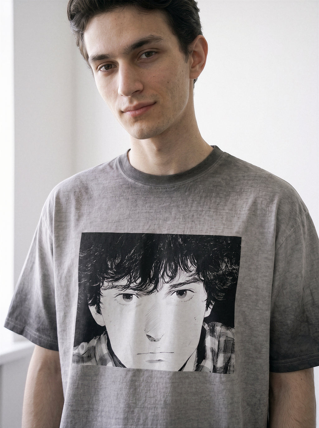 Close-up shot of a model looking down, showcasing the detailed retro manga portrait print on an ombre grey heavyweight boxy fit graphic tee.Showing a face on the front, set against a plain light background.