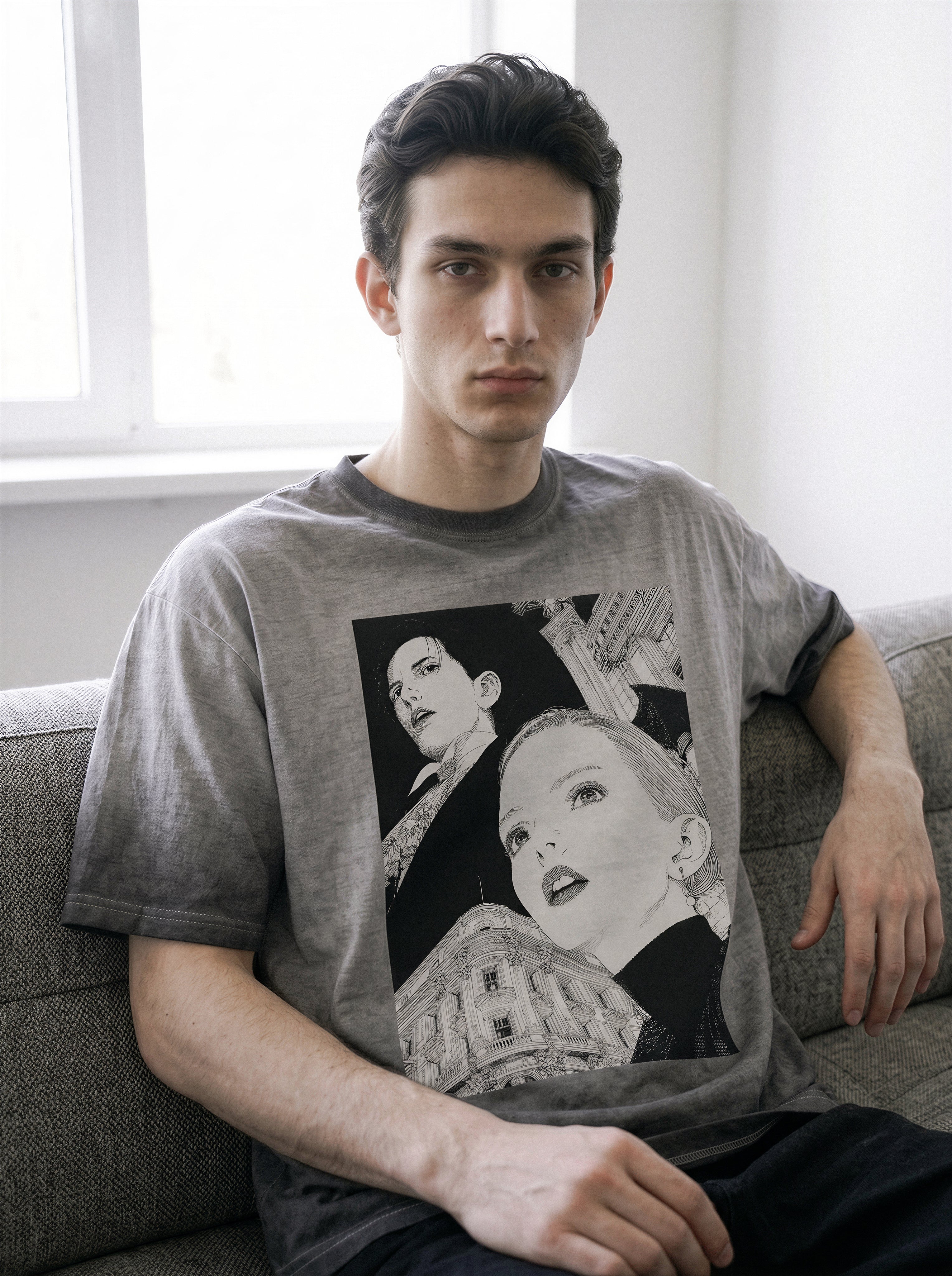 Model resting his hand on his neck while sitting, demonstrating the fit of an ombre grey retro manga graphic tee in a premium heavyweight cotton.