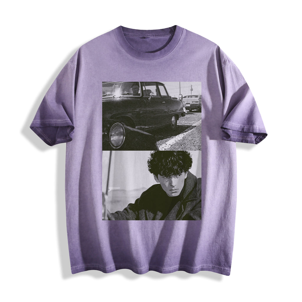 Flat lay product photography of an ombre violet heavyweight boxy fit t-shirt highlighting a gritty 90s monochrome split-panel print of a vintage car and a hardboiled character.