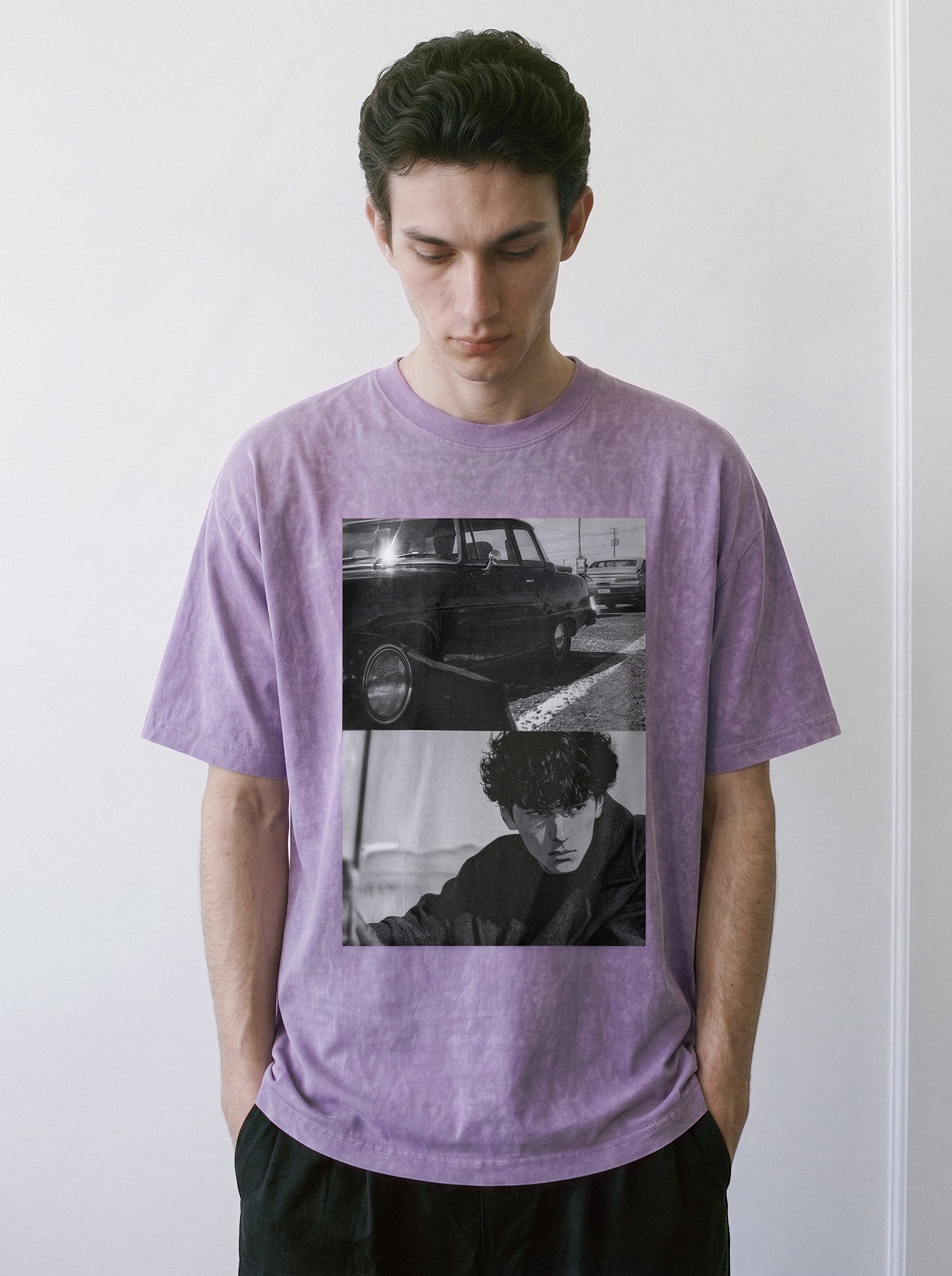 A man standing in a relaxed posture, wearing an ombre violet oversized boxy fit graphic tee featuring a gritty monochrome split-panel cinematic design.