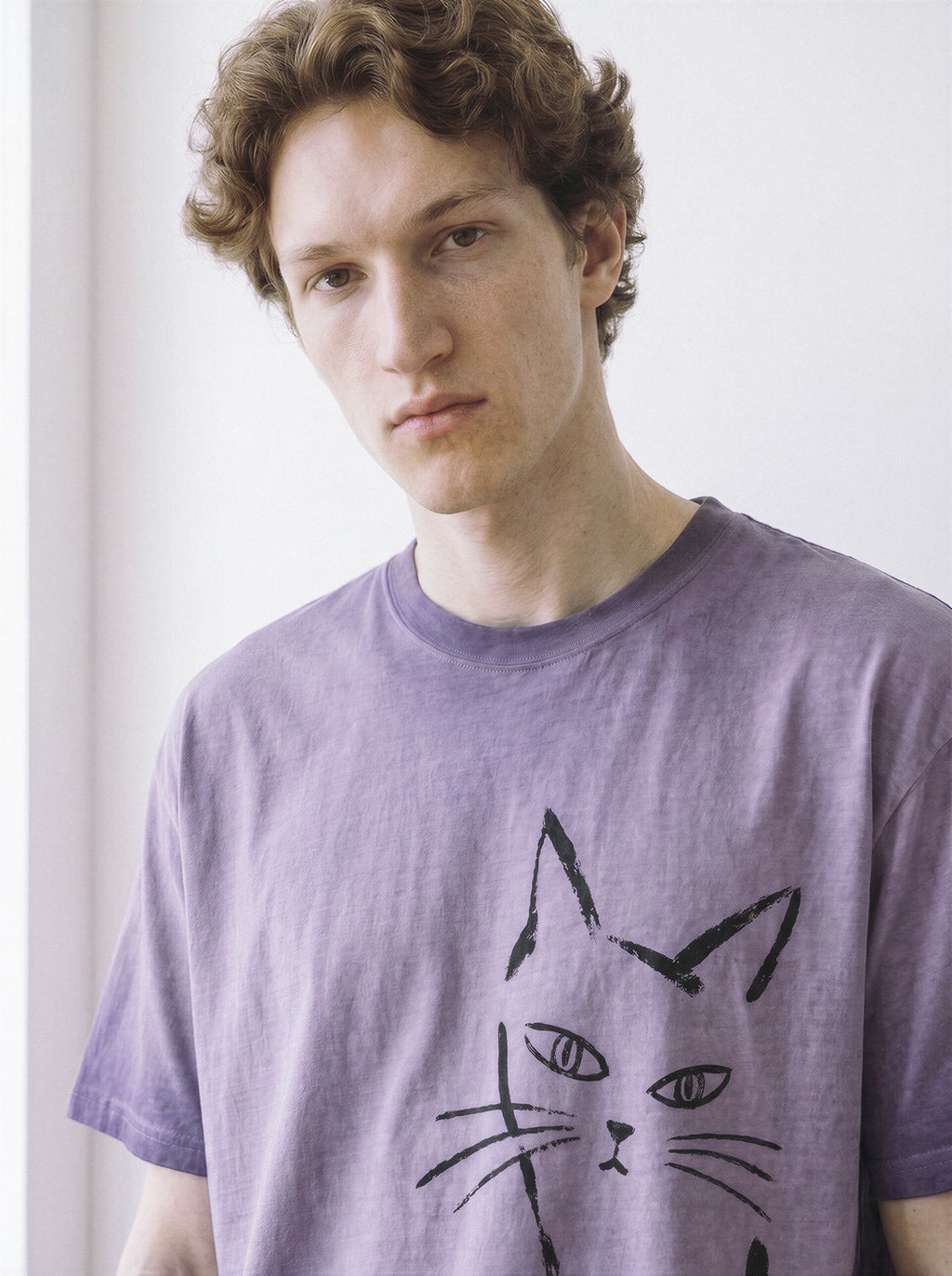 Close-up shot of a male model wearing an ombre violet heavyweight boxy fit t-shirt, emphasizing the minimalist black paint stroke judgmental cat graphic.