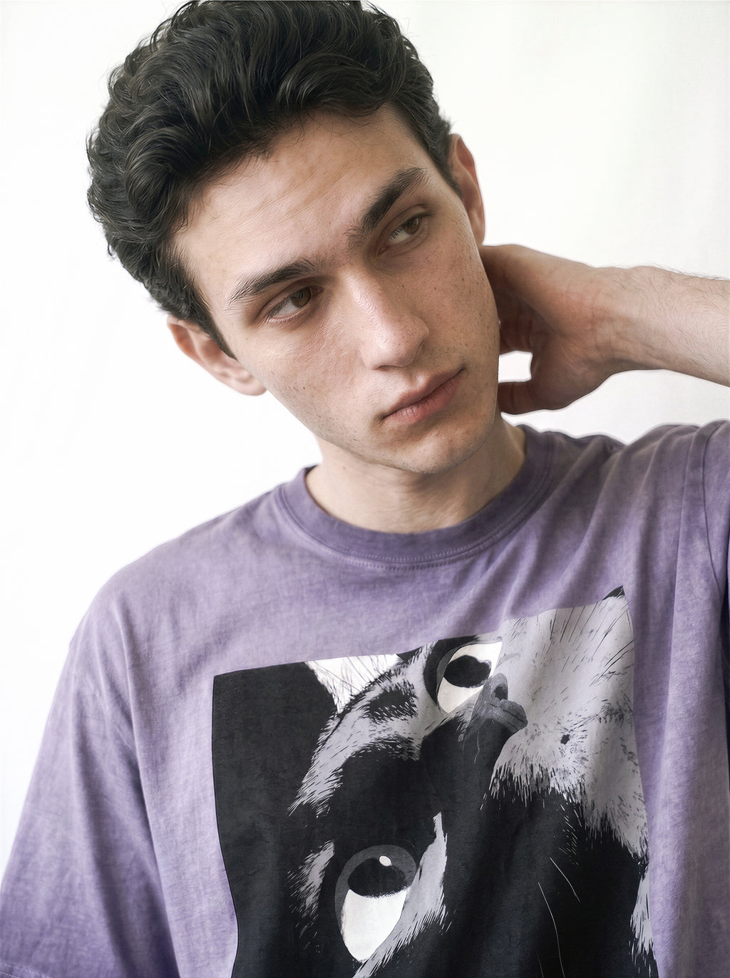 Close-up upper body portrait of a male model with a tilted head pose, emphasizing the monochrome manga freeze-frame staring eyes print on an ombre violet tee.