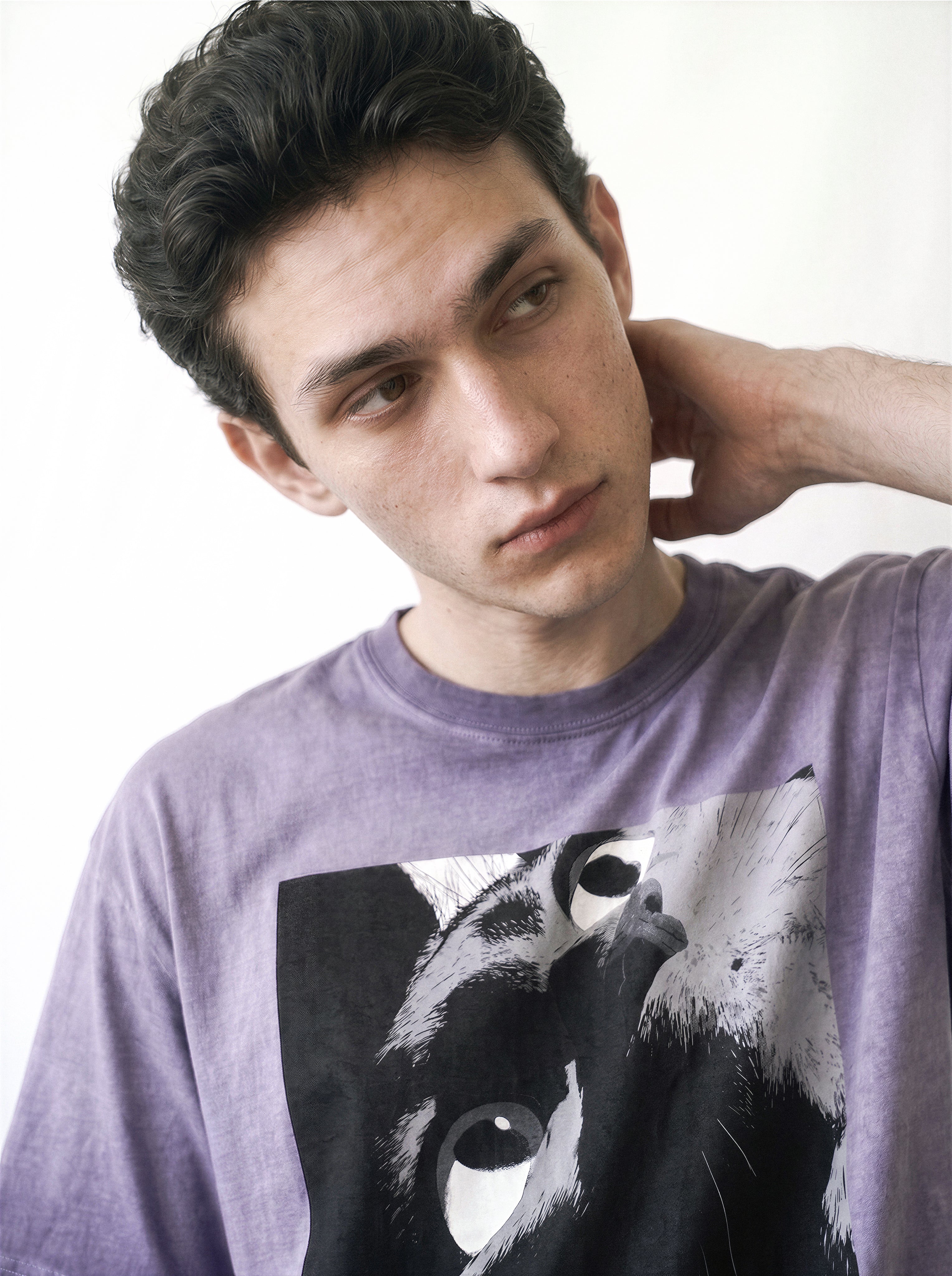 Close-up upper body portrait of a male model with a tilted head pose, emphasizing the monochrome manga freeze-frame staring eyes print on an ombre violet tee.