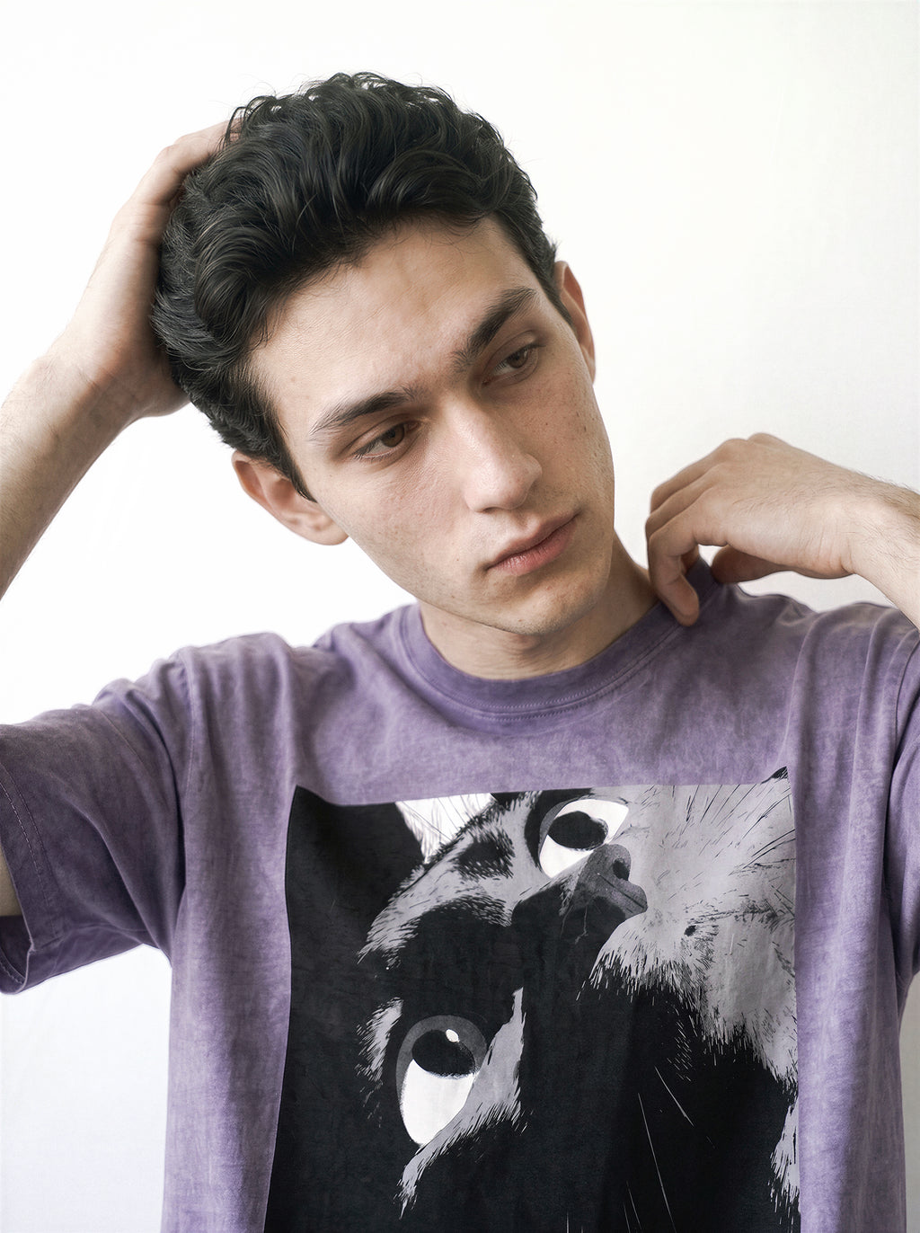 Front view of a male model with his hands behind his head, highlighting the heavy boxy fit of an ombre violet streetwear t-shirt with a striking alternative manga eye graphic.
