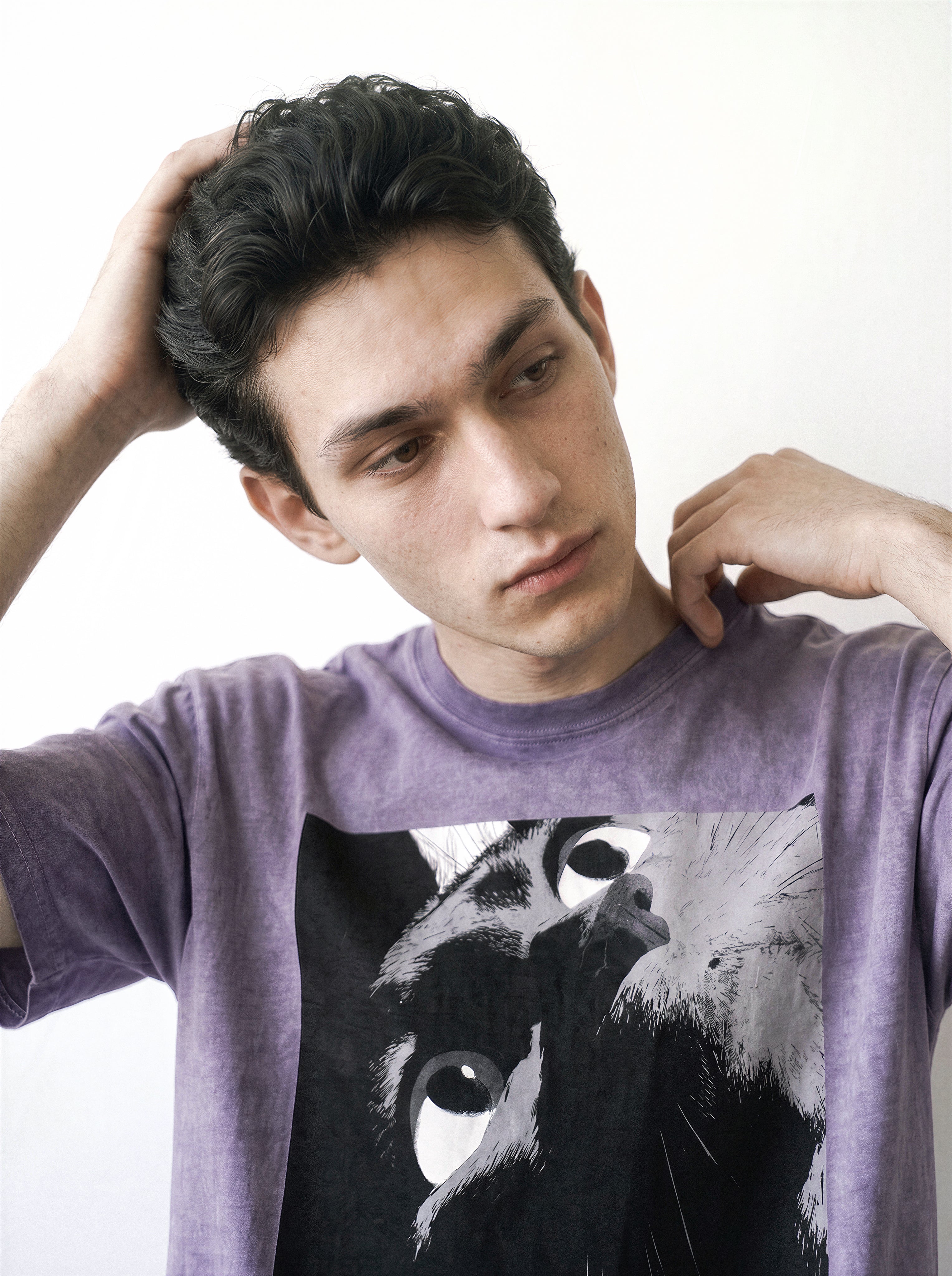 Front view of a male model with his hands behind his head, highlighting the heavy boxy fit of an ombre violet streetwear t-shirt with a striking alternative manga eye graphic.