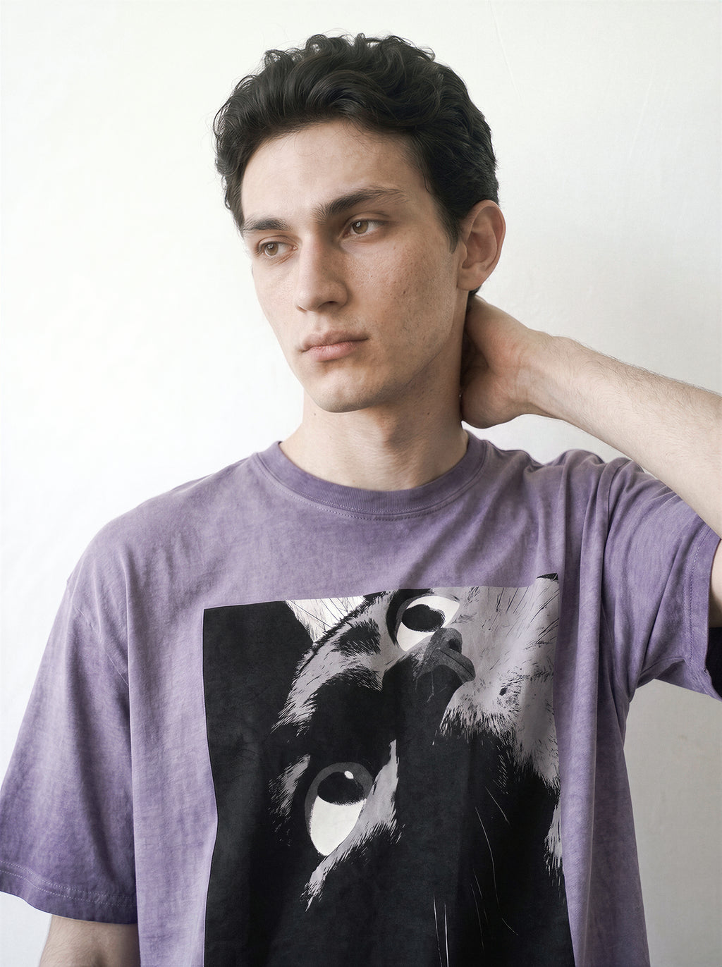 Side angle portrait of a male model with his hand touching his neck, demonstrating the structured drape of an ombre violet heavyweight boxy fit tee with a comic panel graphic.