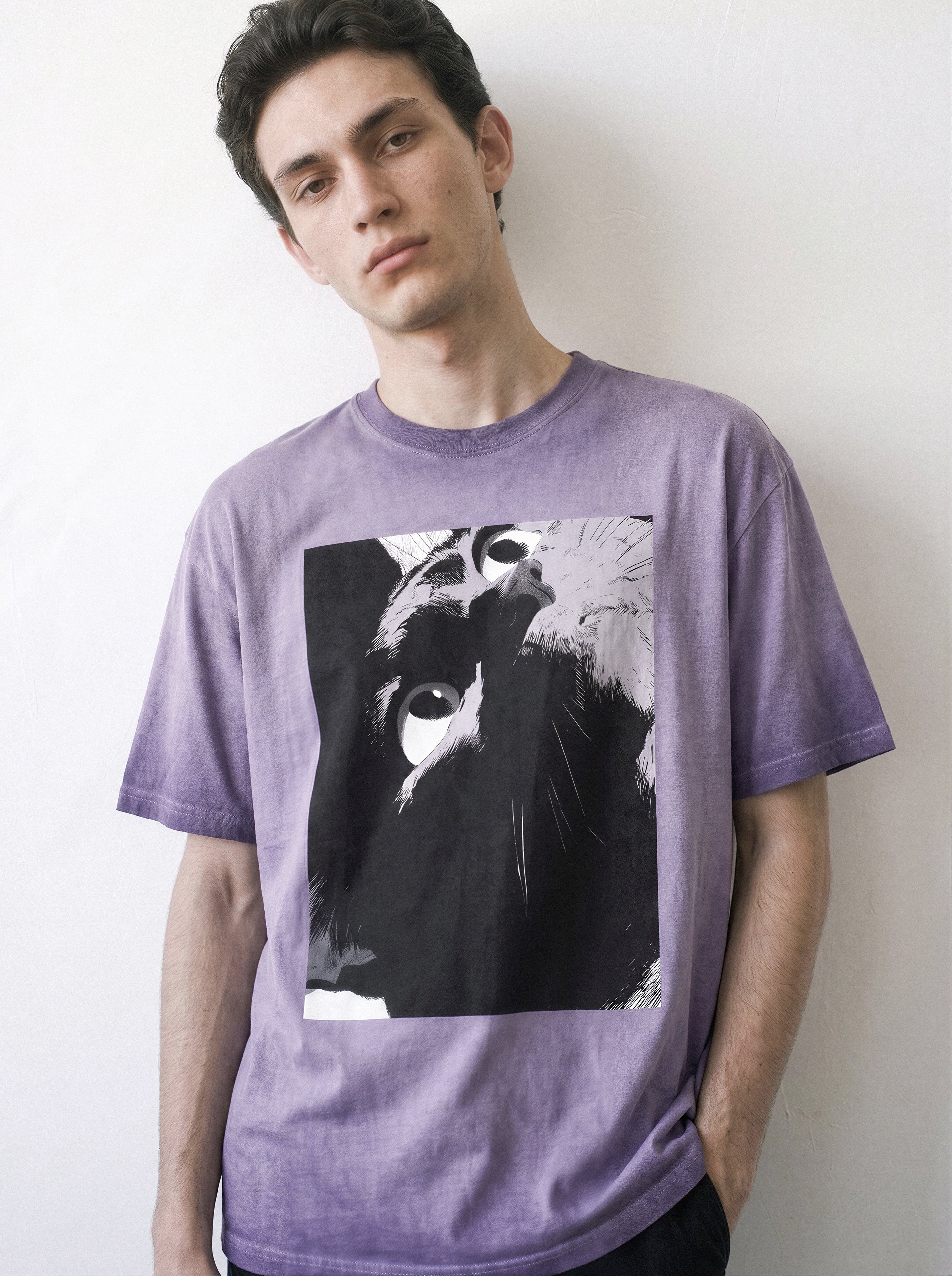 Front portrait of a male model with a tilted head pose, wearing an ombre violet heavyweight boxy fit graphic tee featuring a black-and-white manga freeze-frame close-up of staring eyes.