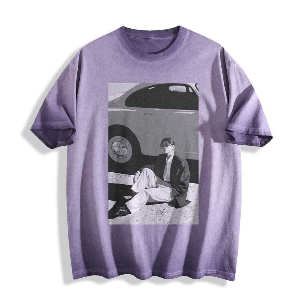 A lavender purple short-sleeve t-shirt with a striking 90s retro black and white photography print of a person sitting next to a vintage car, displayed on a clean white background.