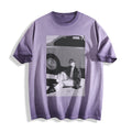 A lavender purple short-sleeve t-shirt with a striking 90s retro black and white photography print of a person sitting next to a vintage car, displayed on a clean white background.