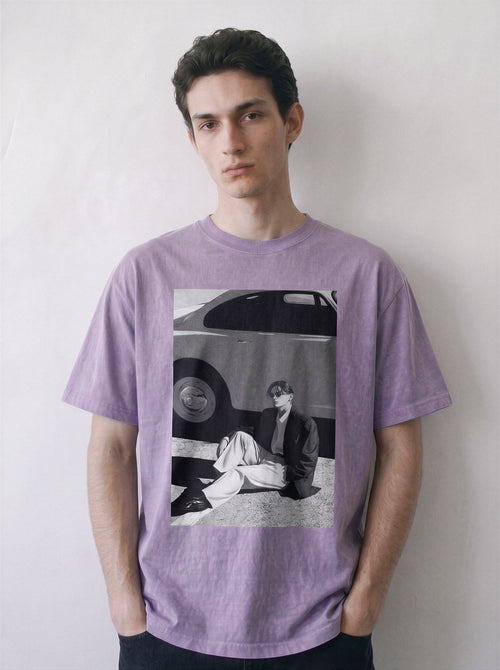 Front view of a model standing with hands in pockets, showcasing the structured silhouette of an ombre violet heavyweight boxy fit t-shirt with a cinematic photography graphic.
