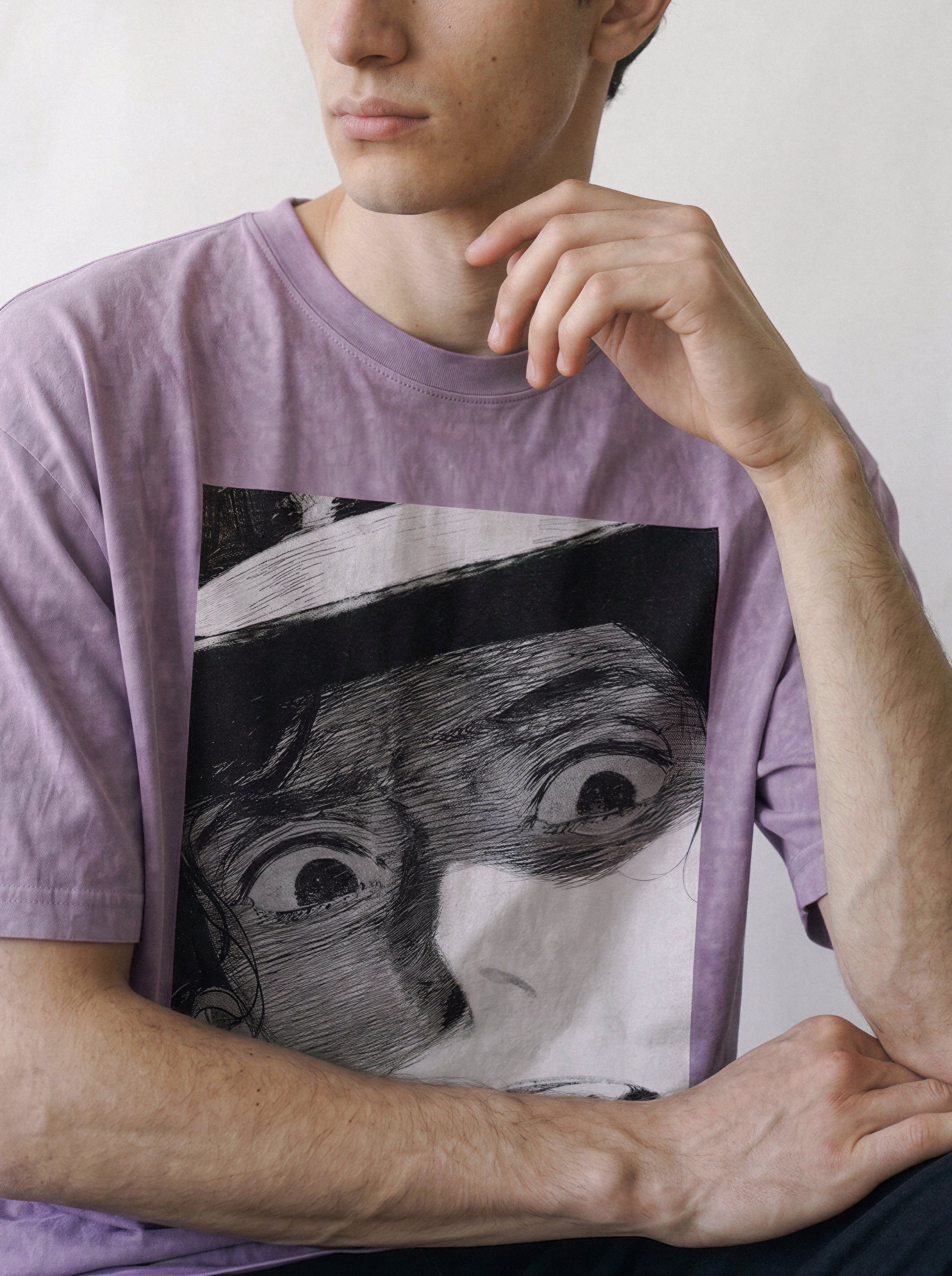 Side angle portrait of a male model with his hand near his chin, demonstrating the structured drape of an ombre violet heavyweight boxy fit tee with a comic panel graphic.