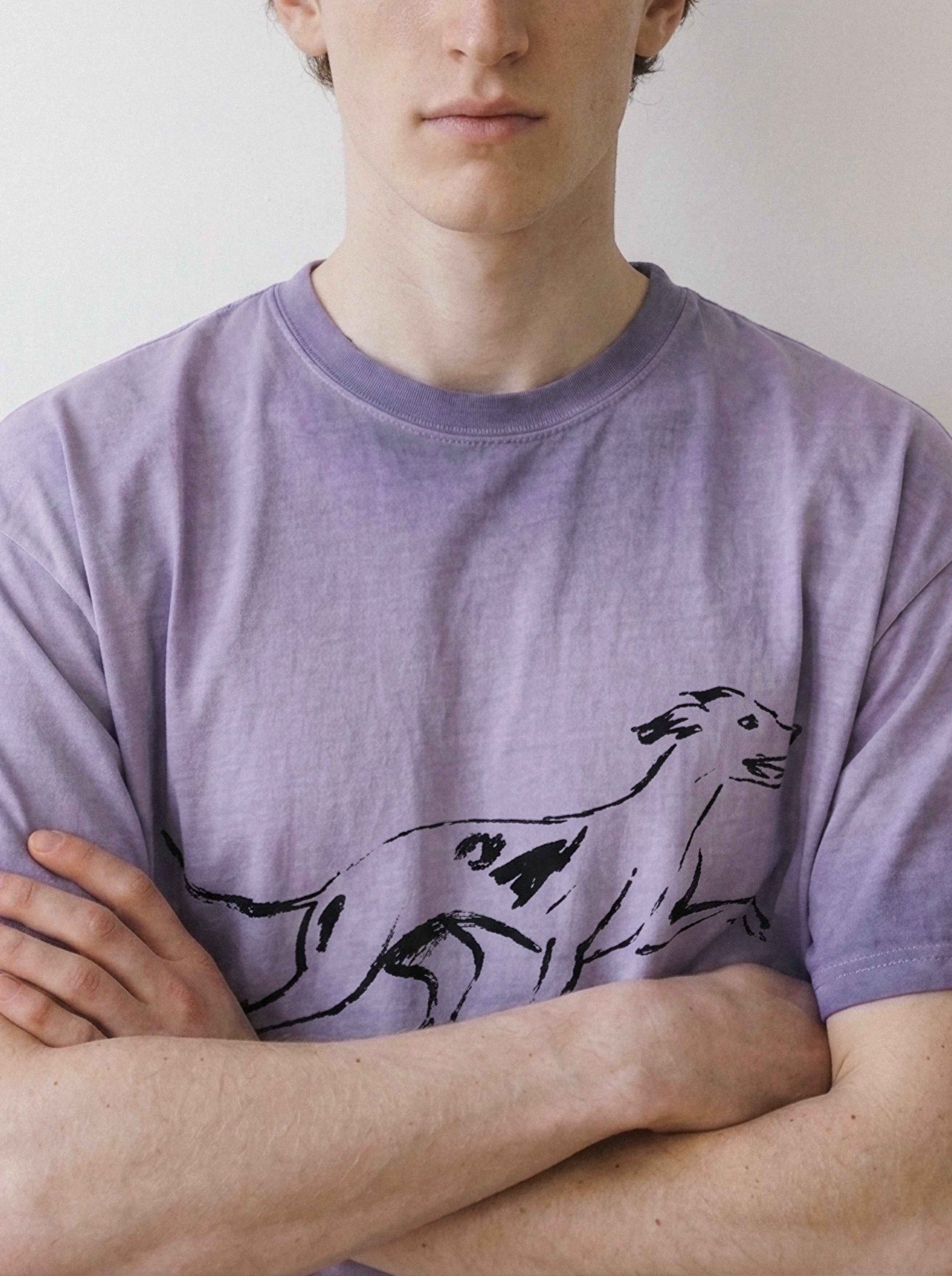 Front view of a model with arms crossed, demonstrating the fit of an ombre violet t-shirt with a striking black running dog line art print.