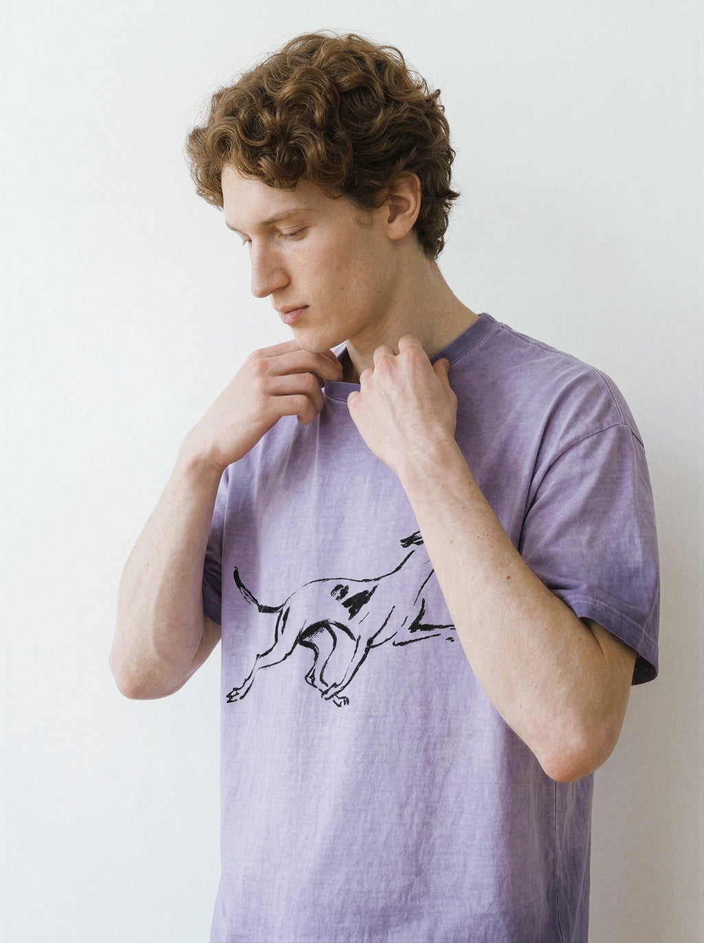 A man wearing a light purple t-shirt with a black line art graphic of a running dog, posing against a plain white wall.