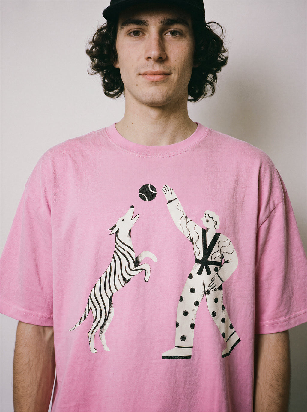 A front view of a male model wearing an aura pink playing fetch ironic graphic tee, highlighting the sarcastic boy and dog illustration and dry humor apparel style.