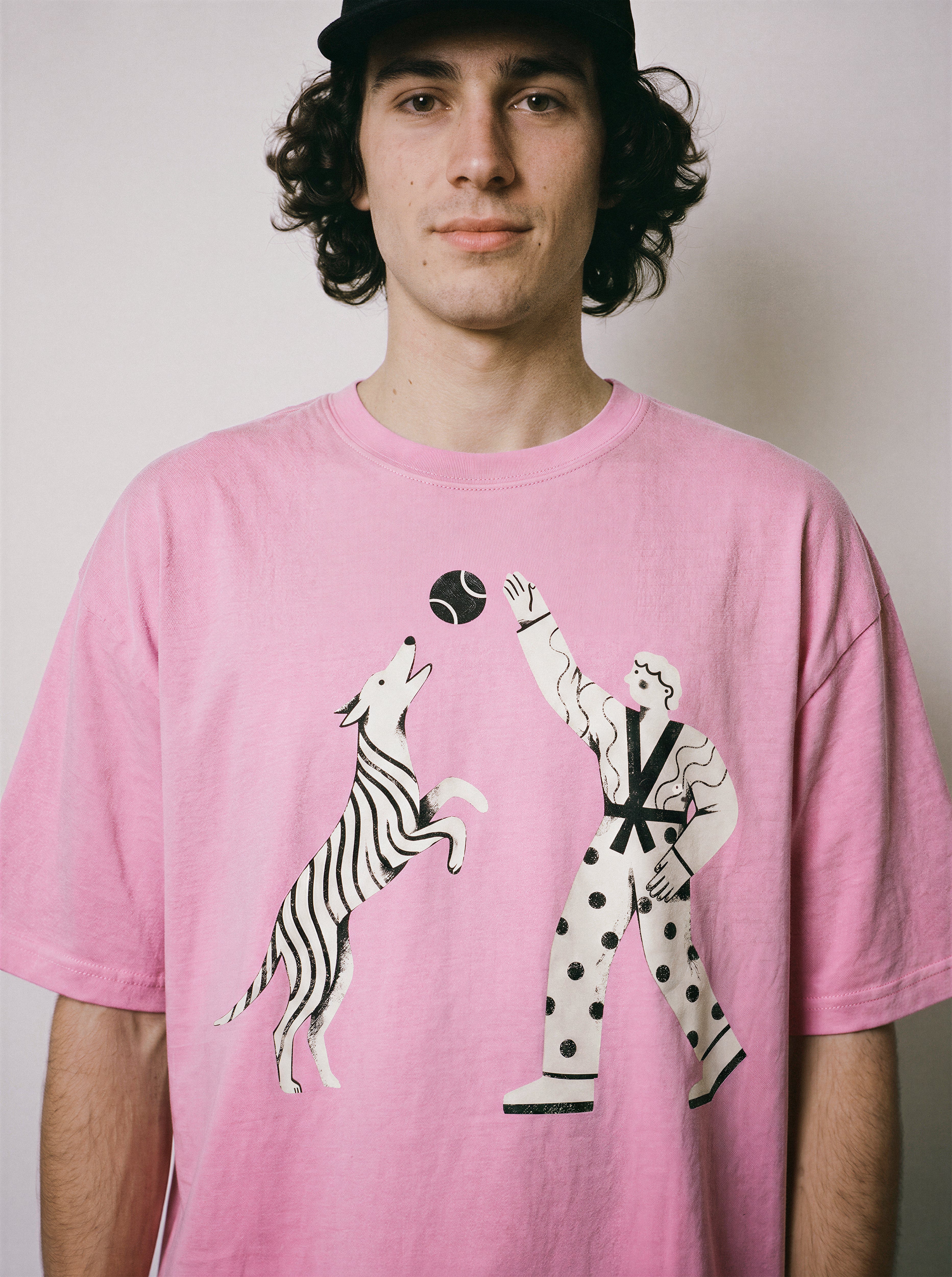 A front view of a male model wearing an aura pink playing fetch ironic graphic tee, highlighting the sarcastic boy and dog illustration and dry humor apparel style.