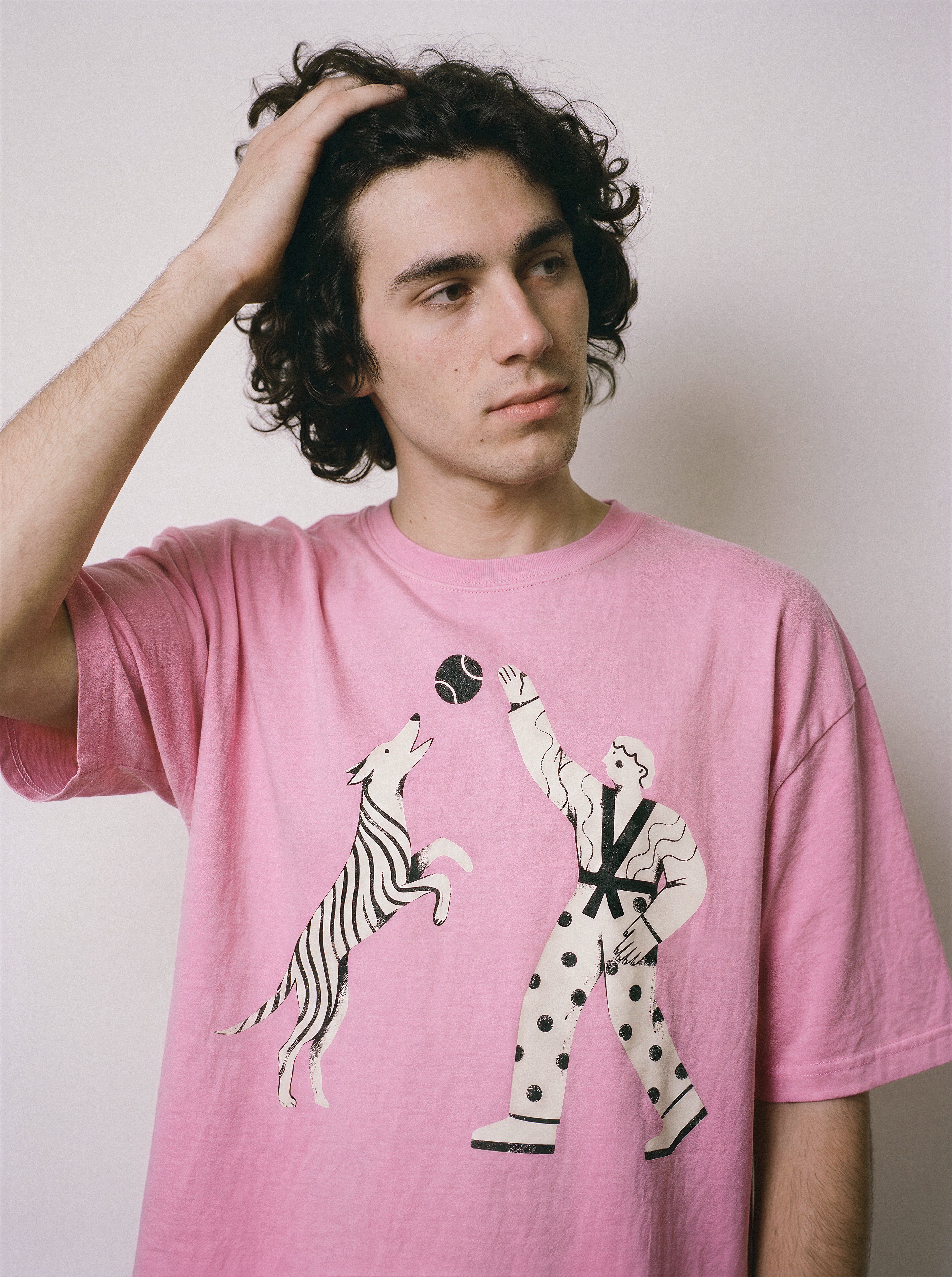 A male model with his hand in his hair wearing an aura pink playing fetch ironic graphic tee, emphasizing the ironic streetwear look and micro-control graphic.