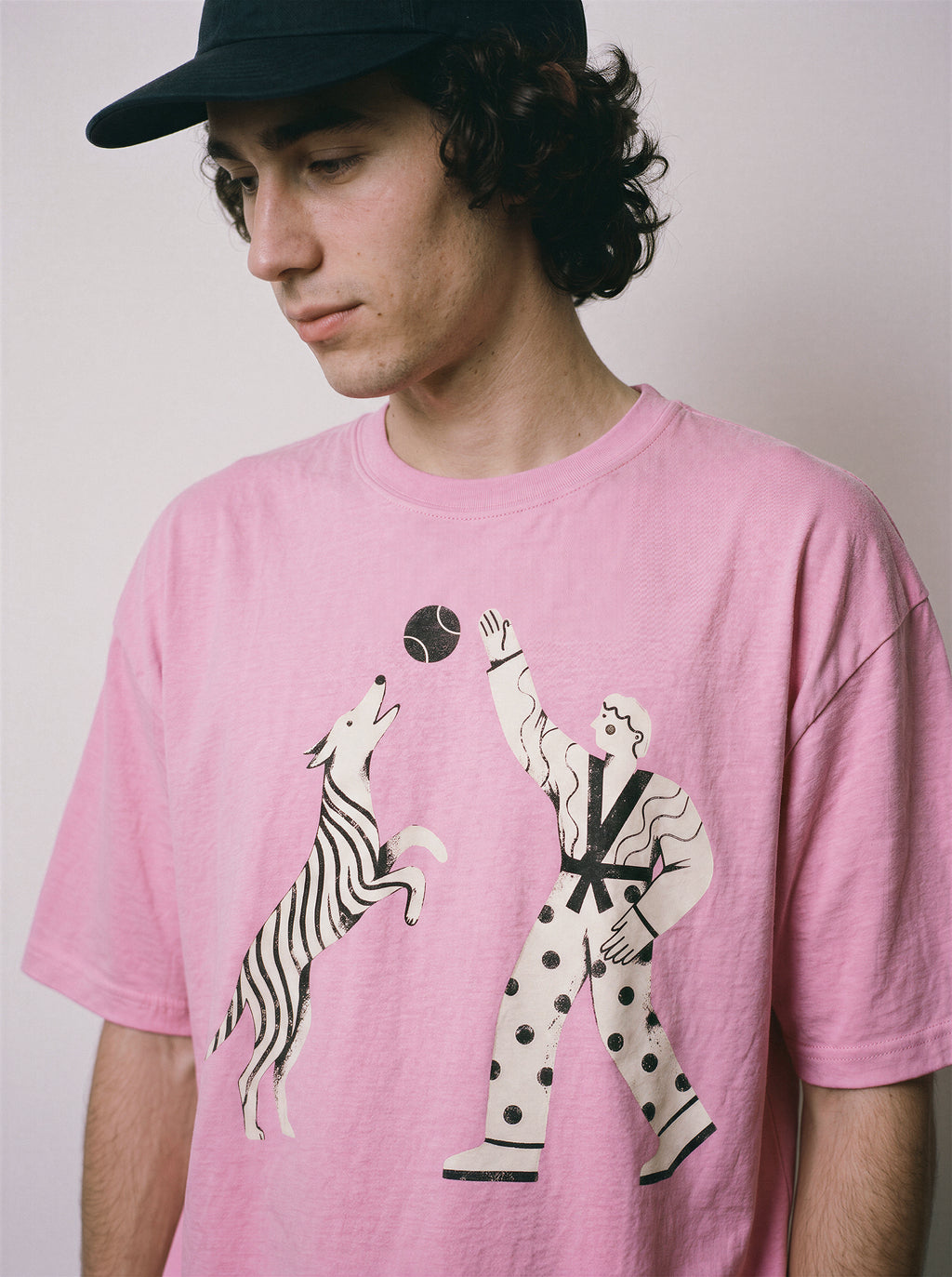 A male model looking down wearing an aura pink playing fetch ironic graphic tee, showcasing the boxy fit and Gen Z existential streetwear vibe.