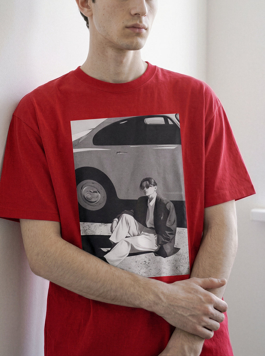 A man wearing a red oversized 90s retro photography graphic T-shirt with a large black and white graphic print on the front showing a vintage car and a seated figure.