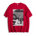 Flat lay product view of a red oversized streetwear t-shirt featuring a 90s retro cinematic black and white photography print, showing a person sitting next to a car. 