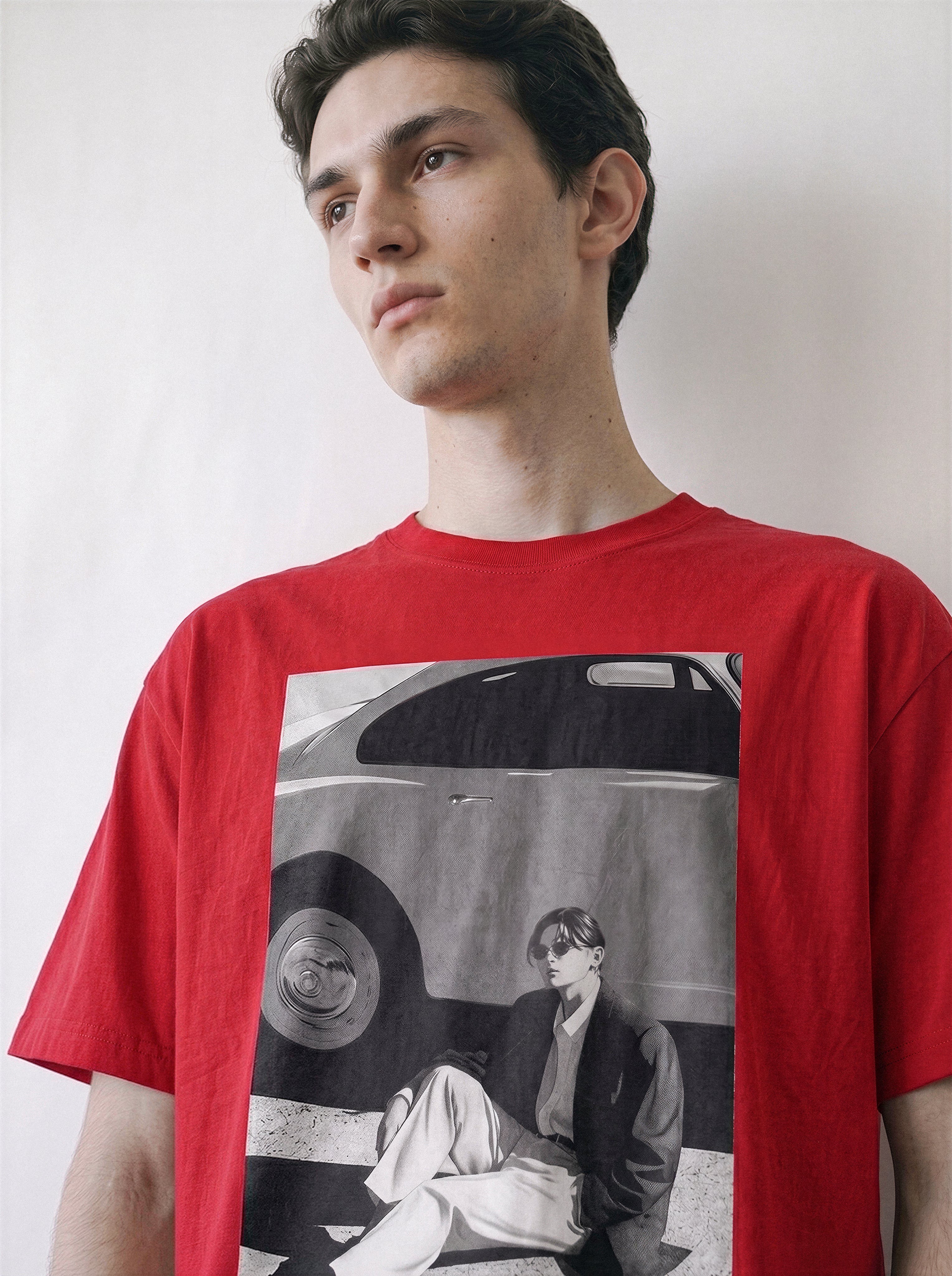 A man wearing a red crewneck t-shirt,clearly displaying the 90s retro cinematic black and white photography print of a vintage car and a seated figure.