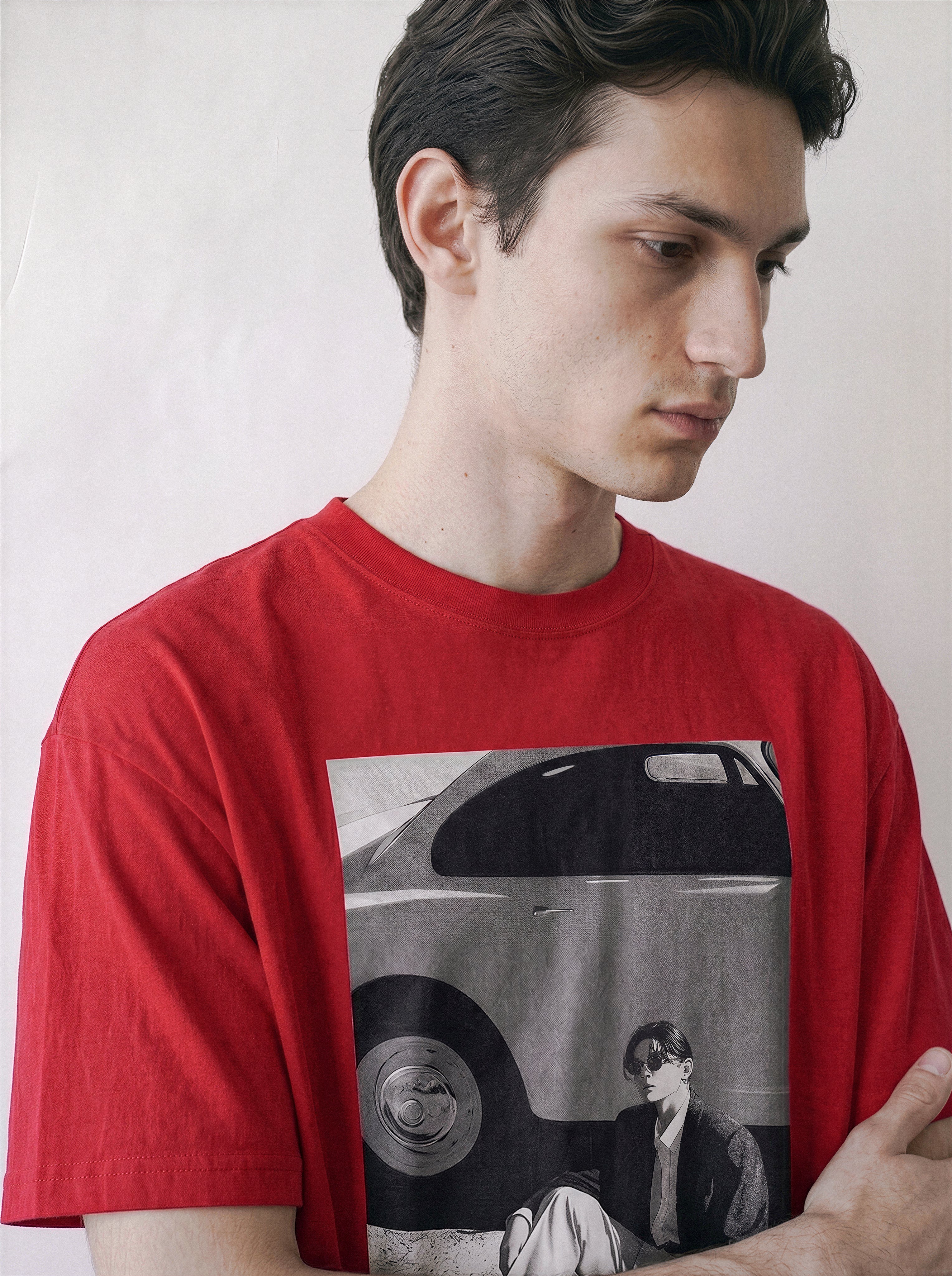 Detailed view of a man looking down, wearing a red oversized indie streetwear t-shirt with a vintage black and white photography print on the front depicting a vintage car and a seated figure, set against a plain off-white background.