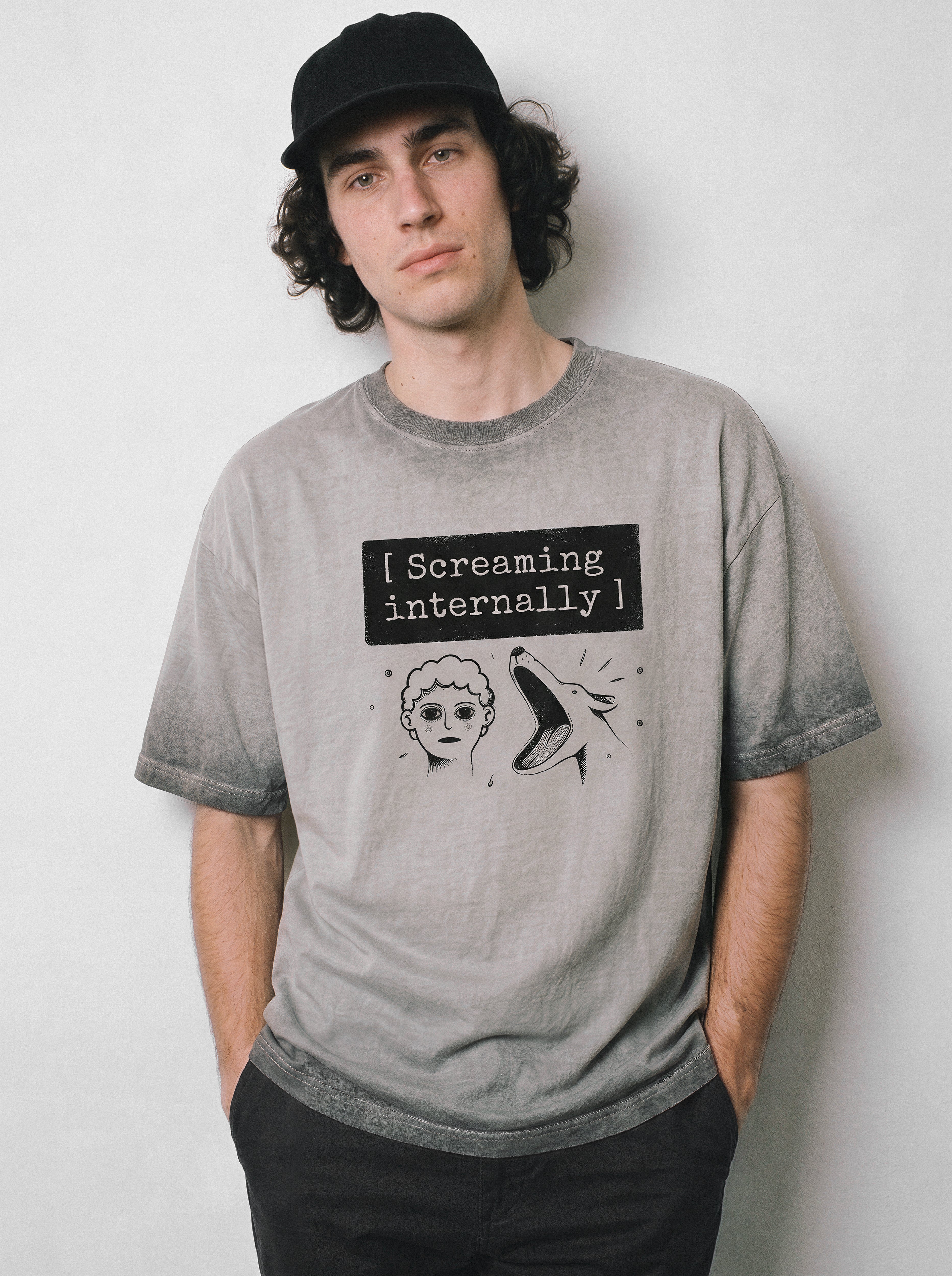 A front view of a male model wearing an ombre grey screaming internally ironic graphic tee, highlighting the text box graphic and relatable silent meltdown aesthetic.