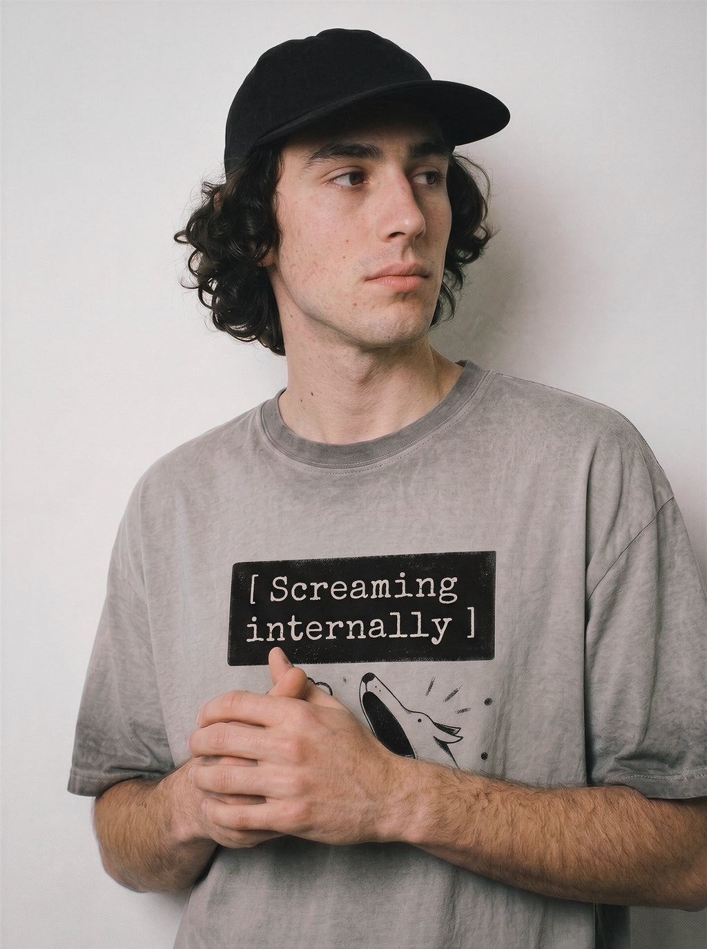 A male model with hands clasped wearing an ombre grey screaming internally ironic graphic tee, demonstrating the quirky illusion of control and dry humor design.