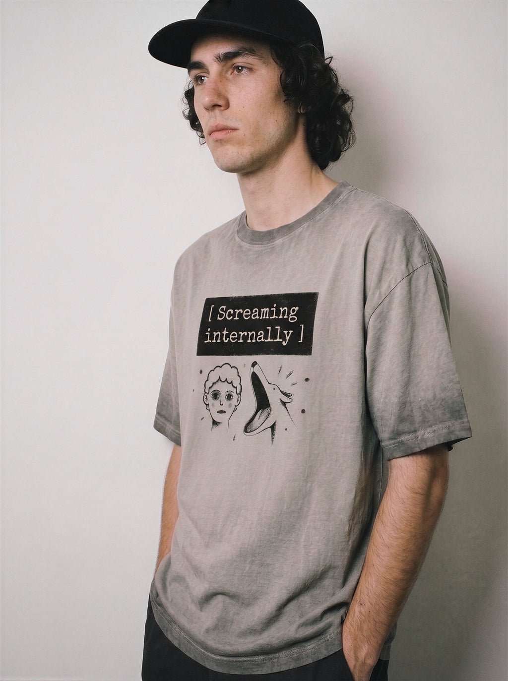 A male model leaning back wearing an ombre grey screaming internally ironic graphic tee, emphasizing the relaxed boxy fit and sarcastic meme apparel look.