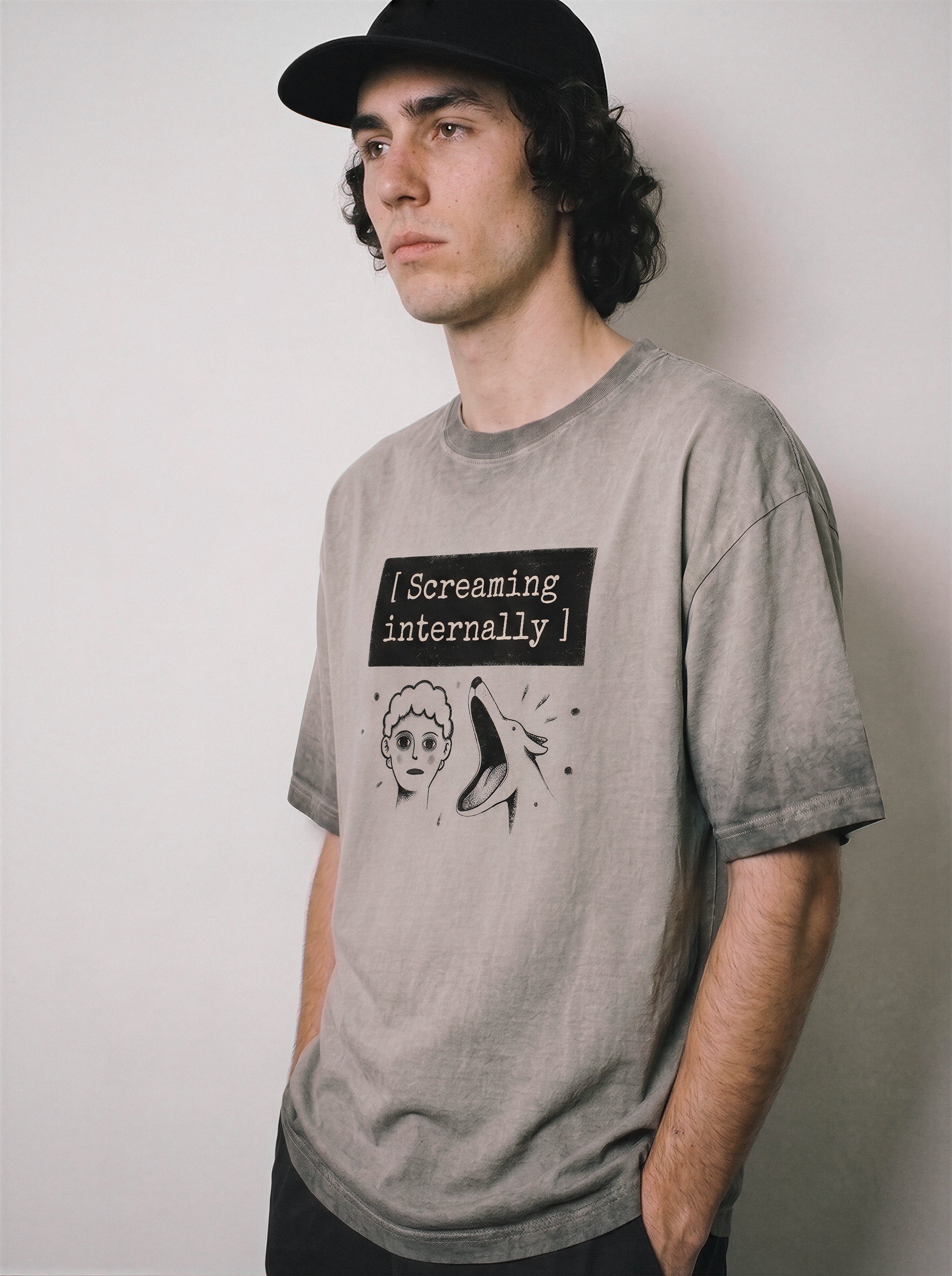 A male model leaning back wearing an ombre grey screaming internally ironic graphic tee, emphasizing the relaxed boxy fit and sarcastic meme apparel look.